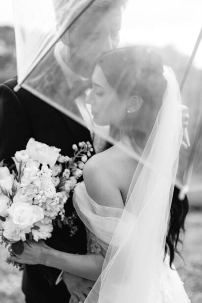 A kiss under a clear umbrella, veil and white bouquet close to the lens