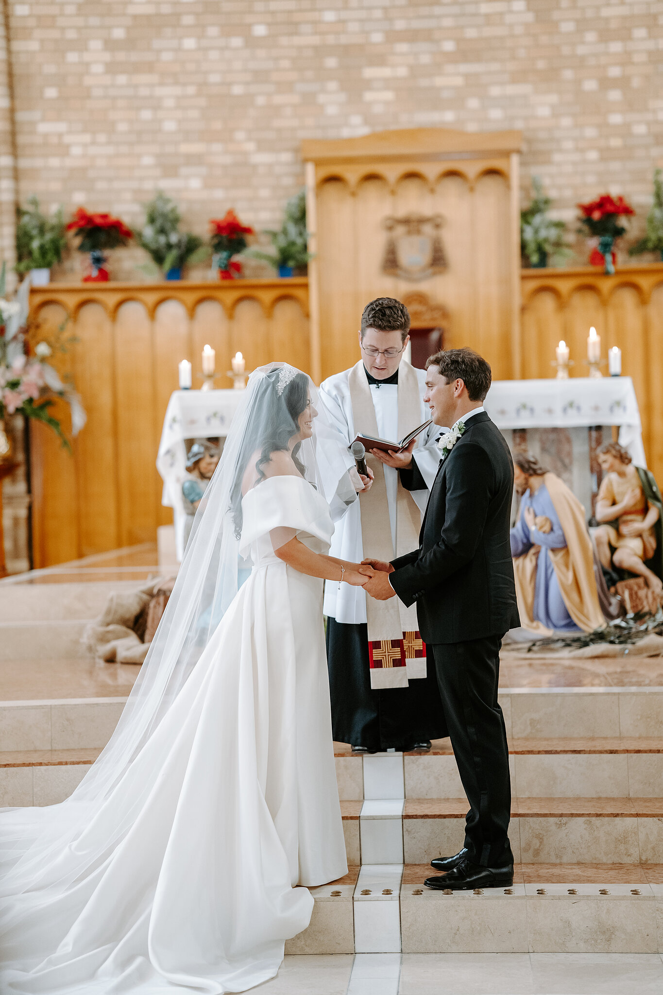 Helena and Xavier hold hands before a priest during their St Christopher’s Cathedral marriage blessing.