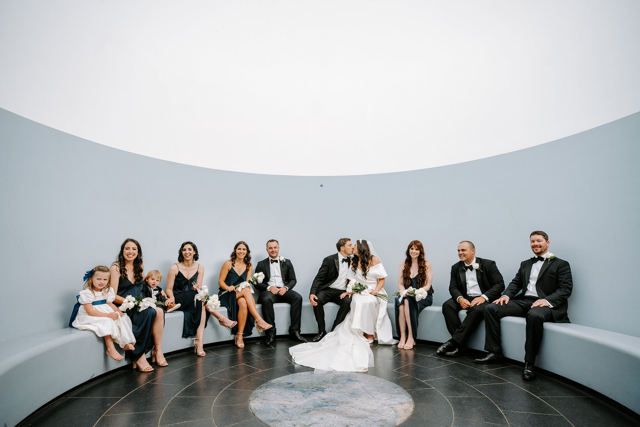 Helena and Xavier kiss among their wedding party inside the Within without Skyspace chamber in Canberra.