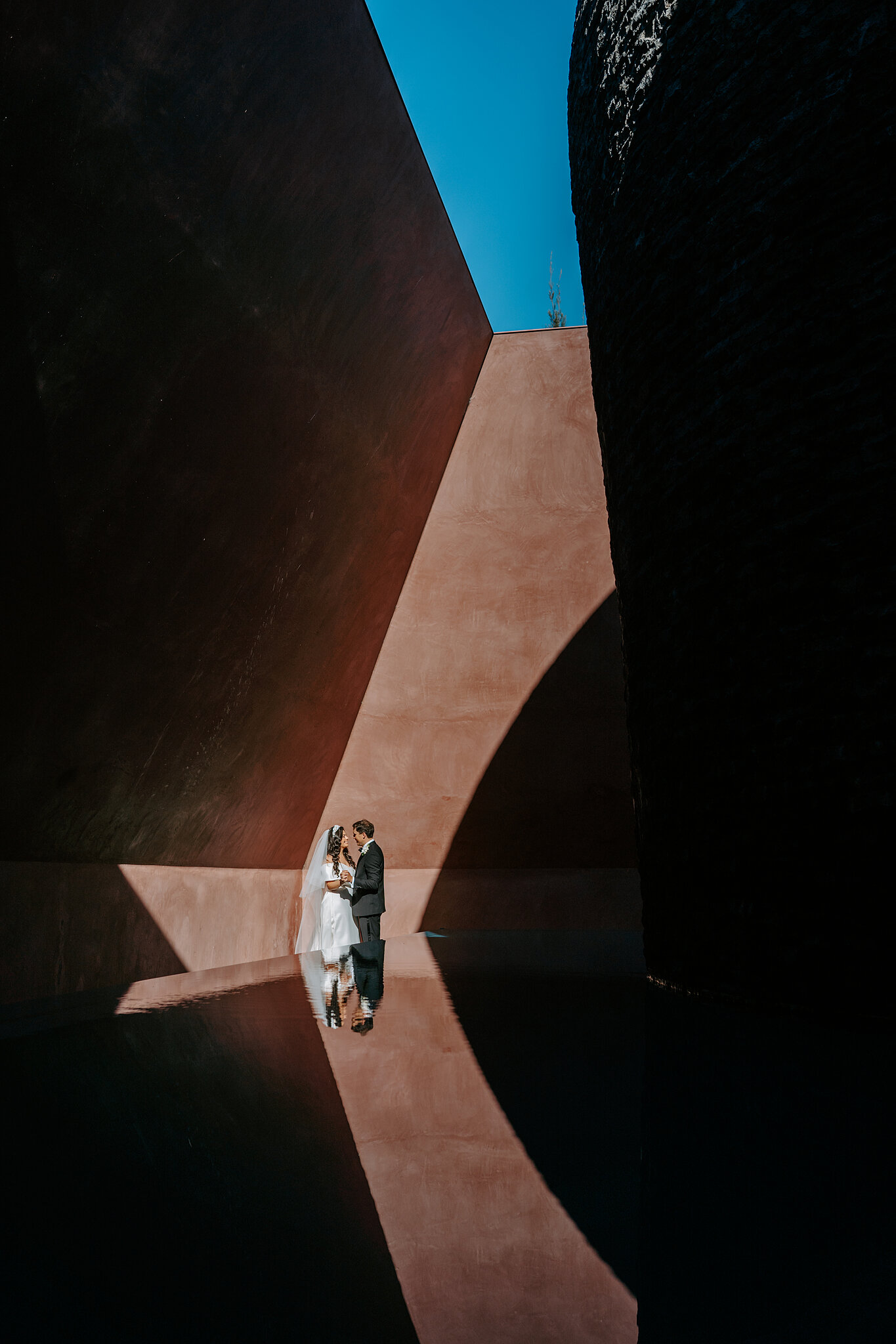 Helena and Xavier reflected in still water between the rust-red walls of James Turrell’s Within without.