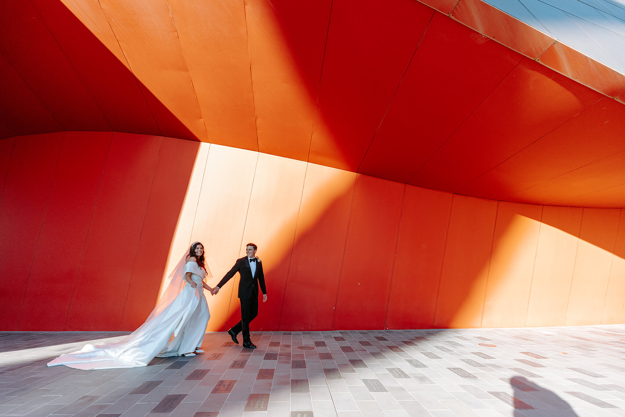 Helena and Xavier hold hands before the National Museum of Australia’s angular orange walls.