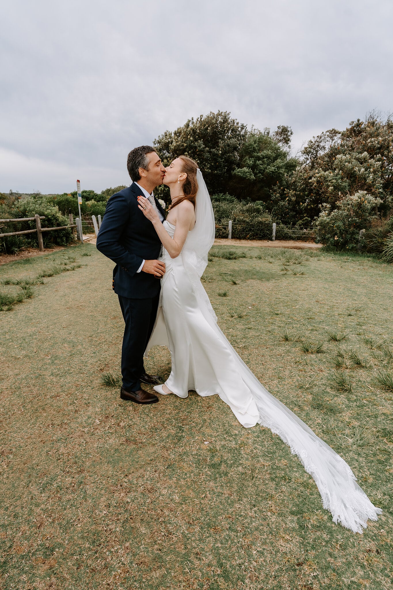 A kiss on the headland lawn beside Horizons South Maroubra, Michele’s veil stretched across the grass.
