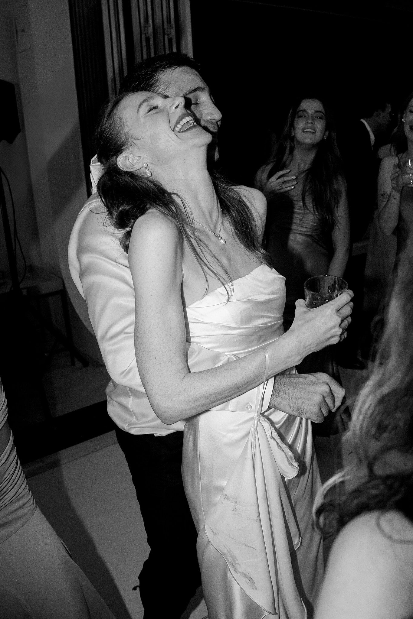 Michele throws her head back laughing in Nico’s arms, drink in hand.
