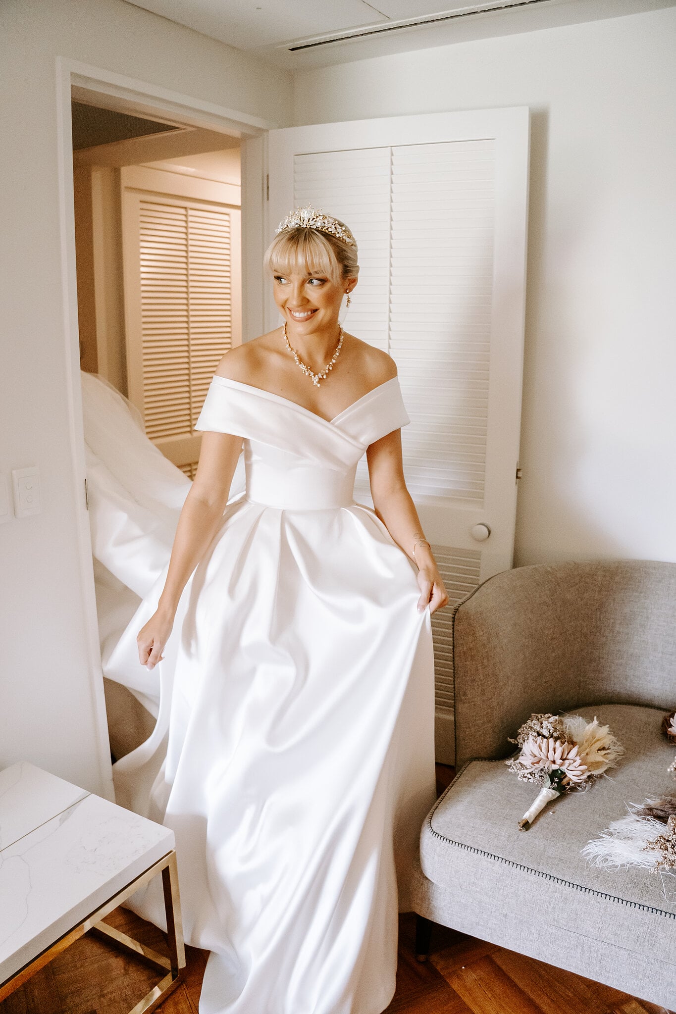 Ashley in her off-the-shoulder satin ball gown and tiara, all smiles in her resort suite.