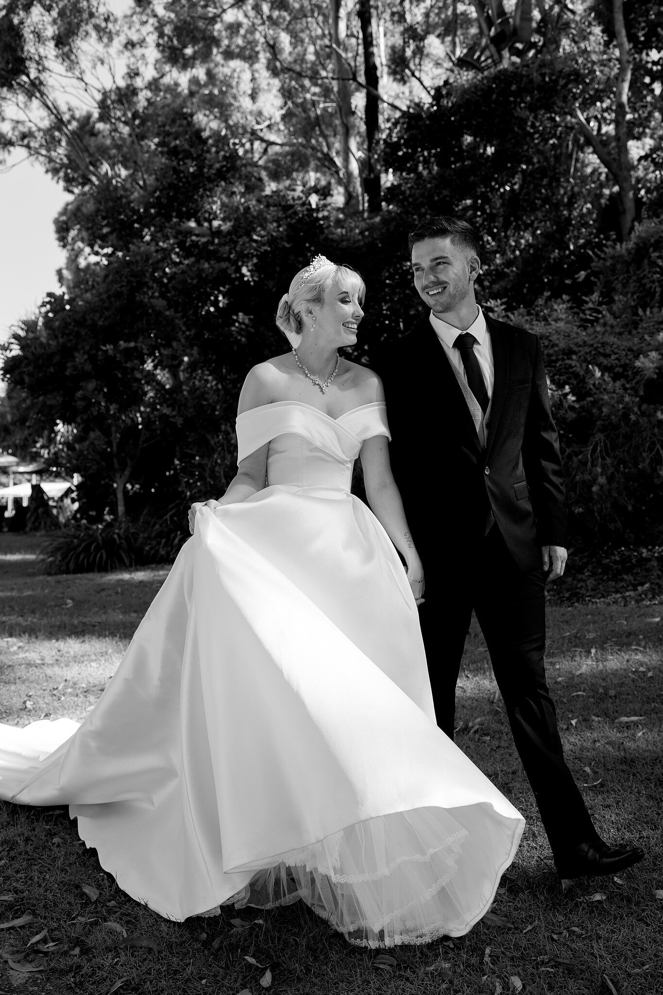 Ashley and Lane share a look as her gown swings through the garden shade.