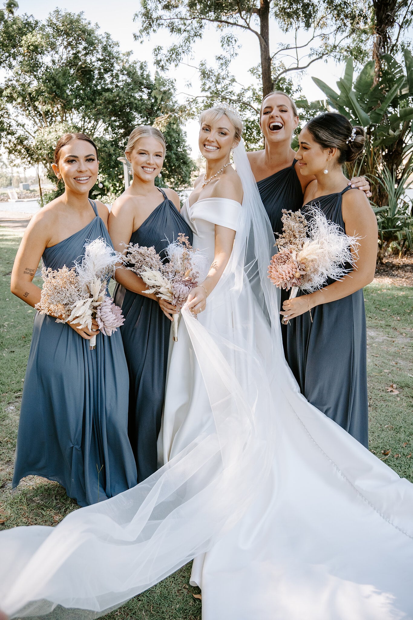 Ashley laughs with her four bridesmaids in navy, dried bouquets in hand.