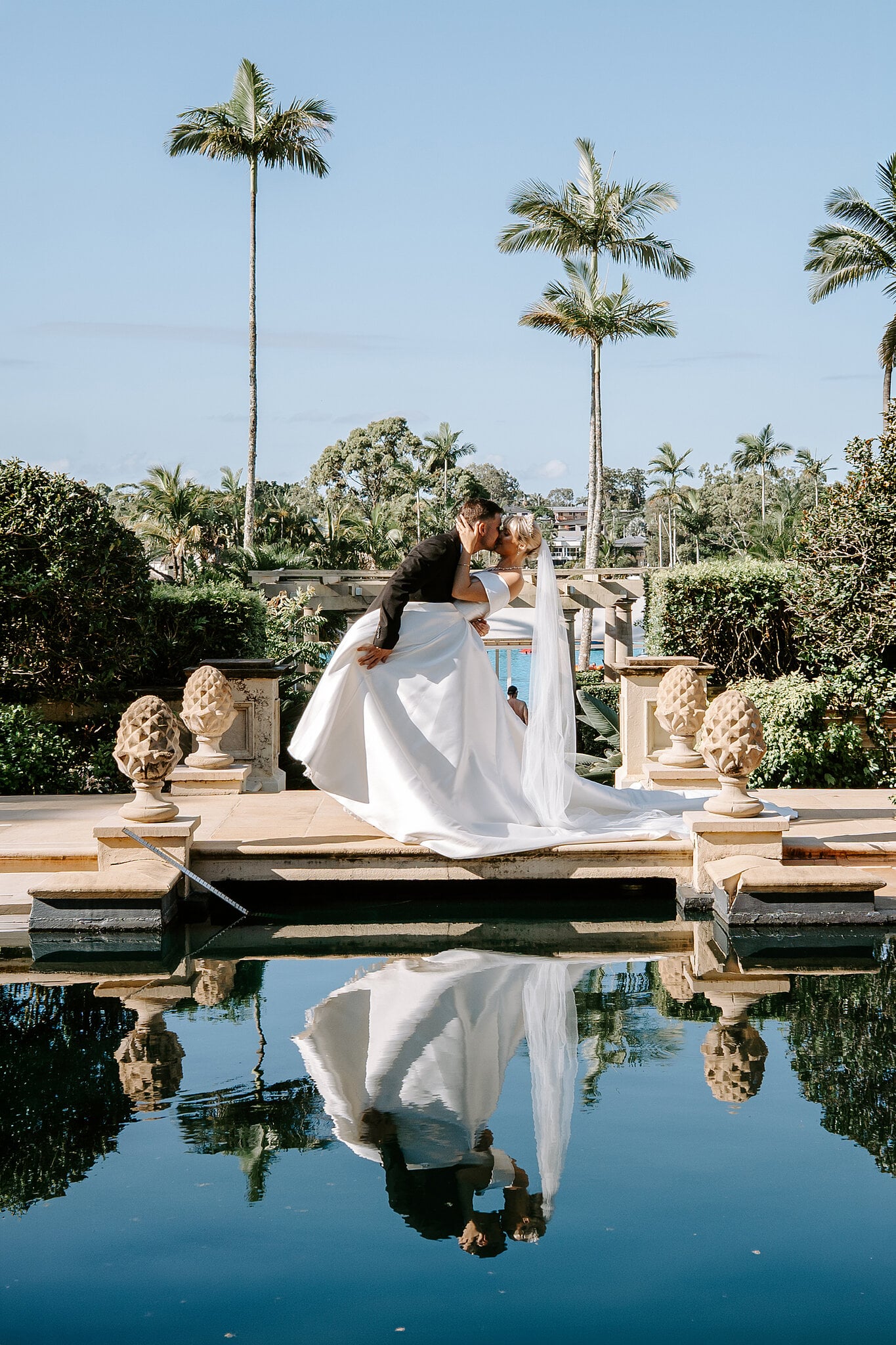 Lane dips Ashley for a kiss beside the reflection pool, palms and stone urns mirrored below.