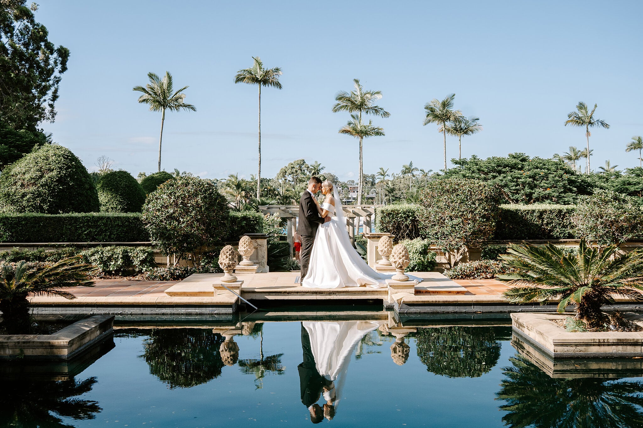 Ashley and Lane beside the formal reflection pool at InterContinental Sanctuary Cove, tall palms overhead.