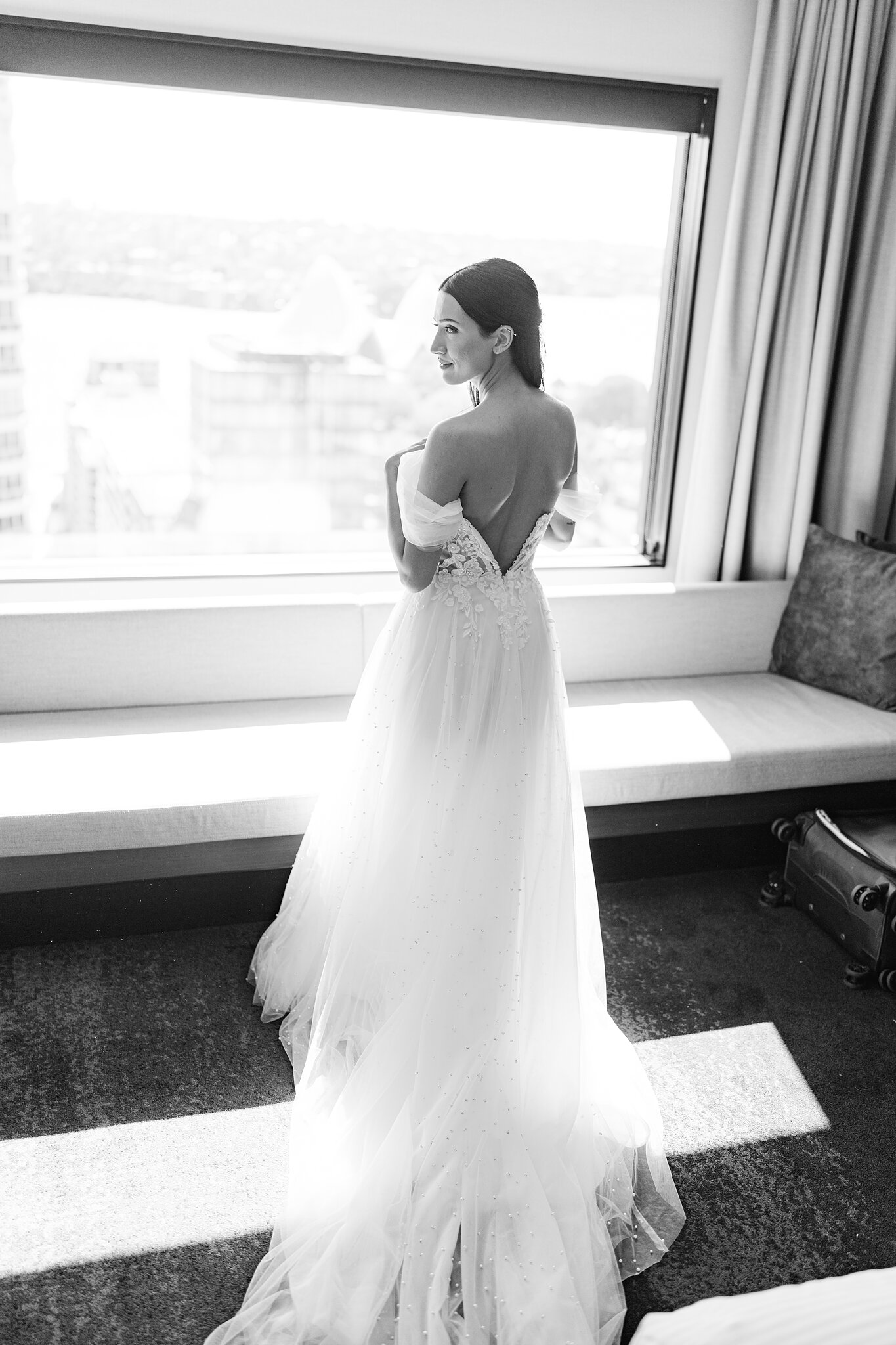 Alexa at the window of her InterContinental Sydney room, the open back of her gown catching the harbour light.