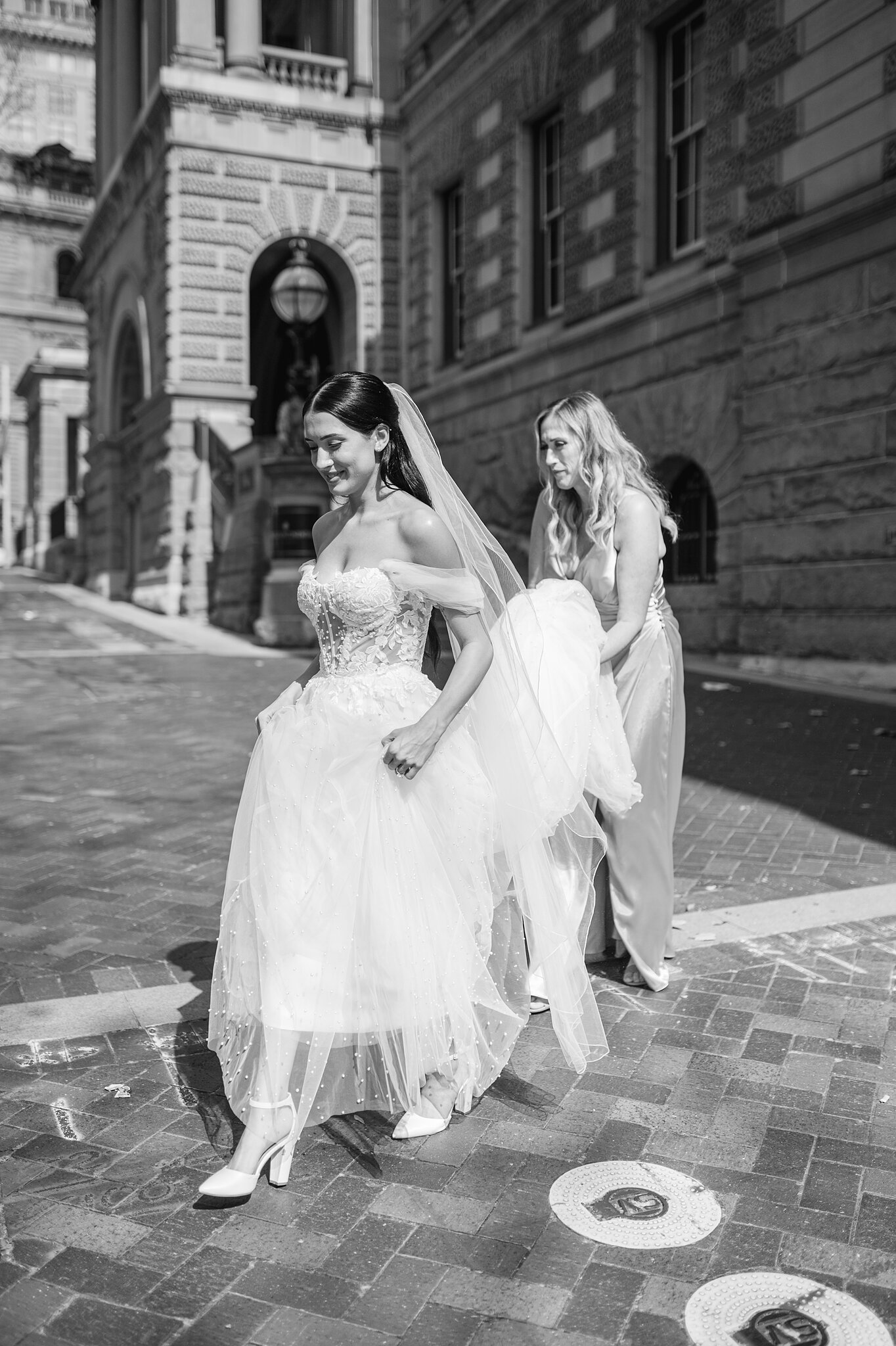 A bridesmaid gathers Alexa’s tulle train as they cross the paved street outside InterContinental Sydney.