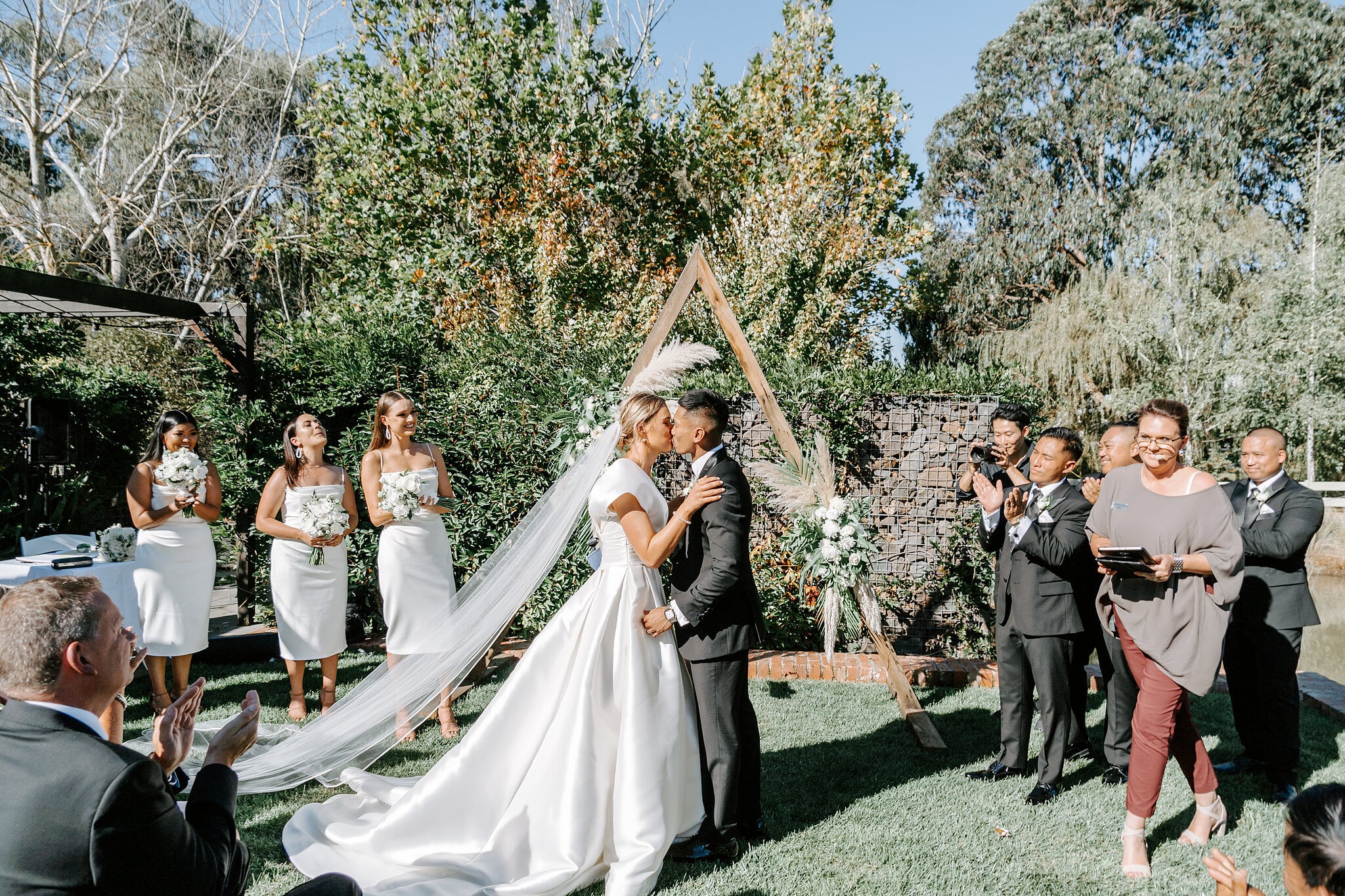 Georgie and Johnny kiss beneath the timber arbour at their Mercure Ballarat garden ceremony.