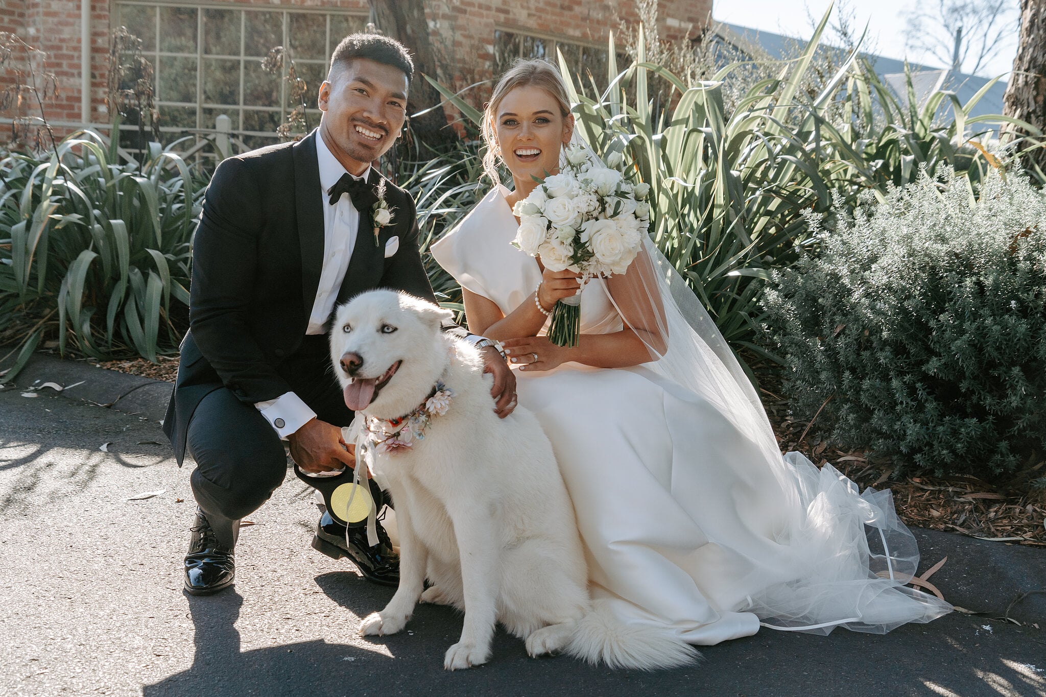 Georgie and Johnny crouch beside their fluffy white dog in its flower collar at Mercure Ballarat.