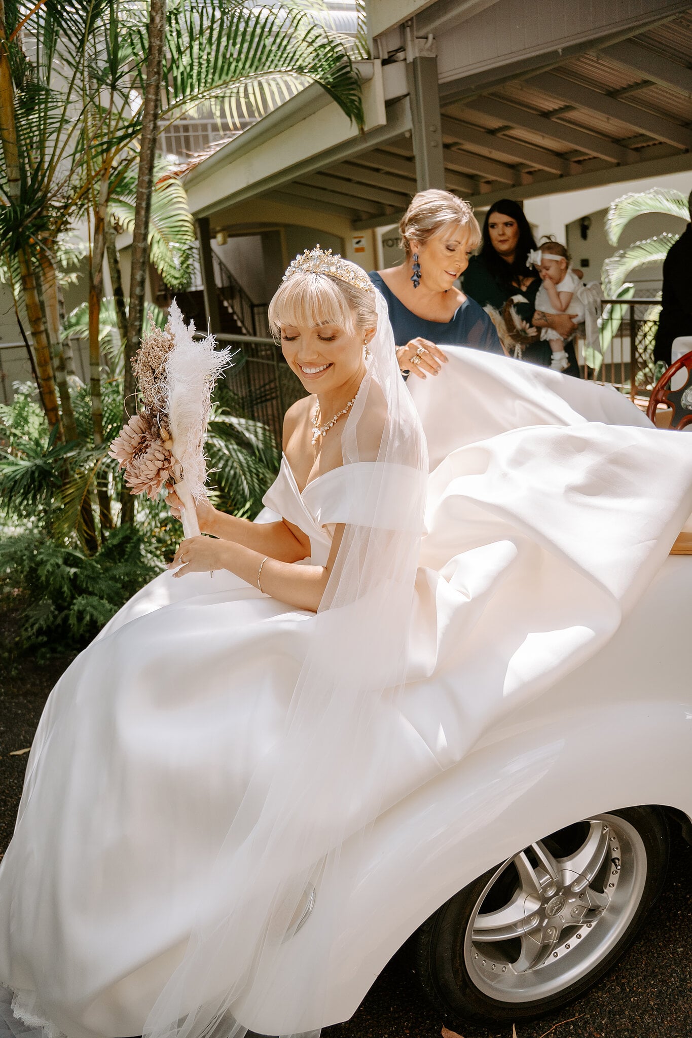 Ashley climbs into a white vintage-style buggy for the ride to the chapel as a loved one gathers her train.