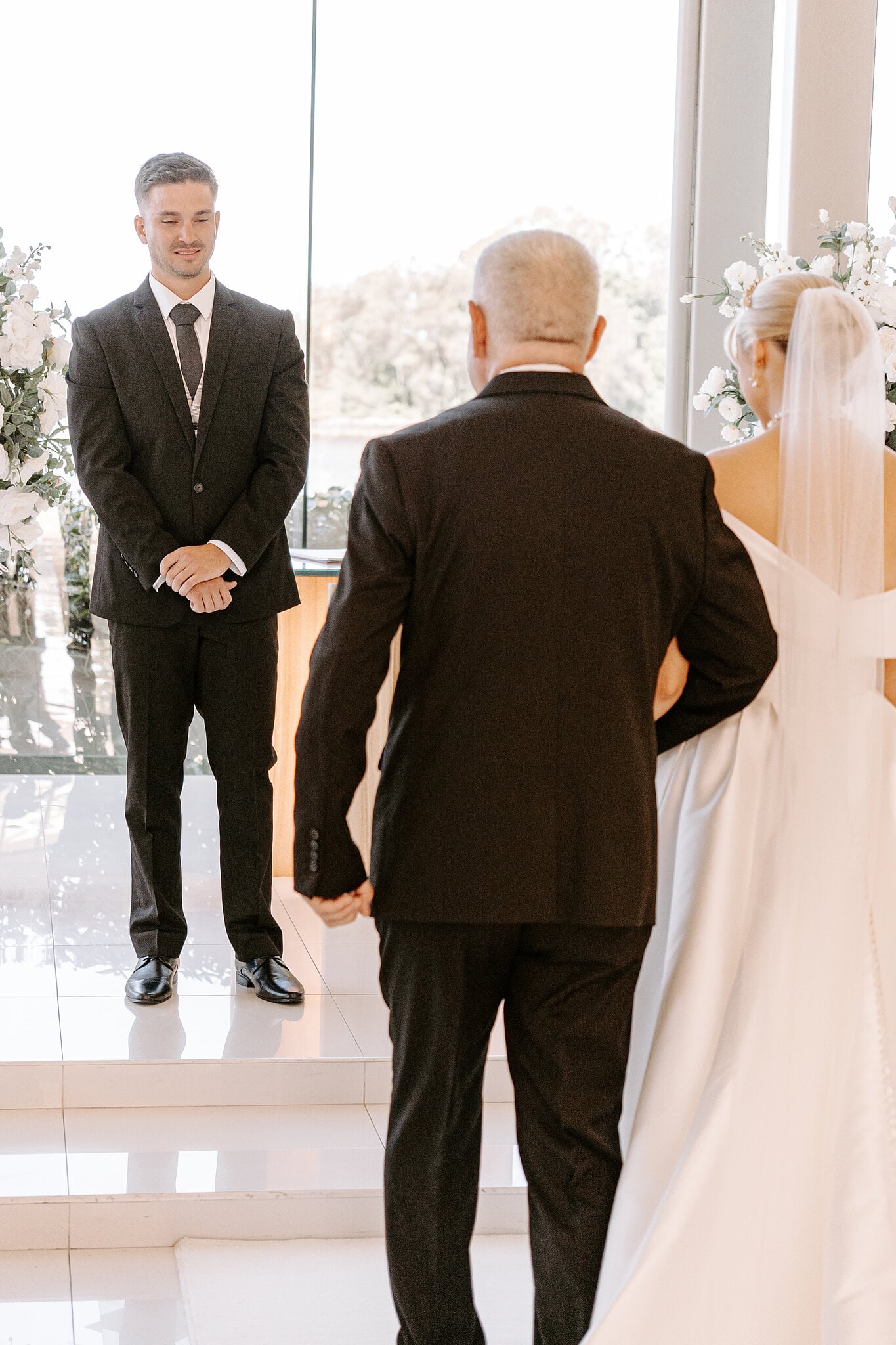 Lane watches Ashley arrive at the top of the aisle inside the glass chapel.