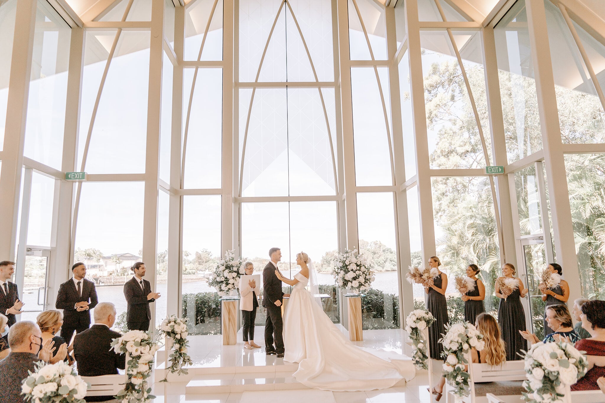 The bridal party and guests cheer the first kiss inside the glass chapel.