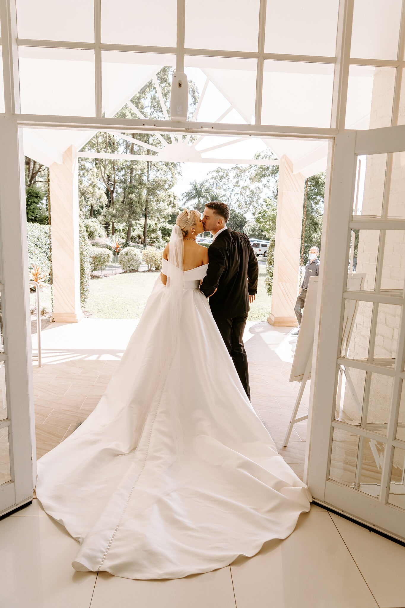 Ashley and Lane pause in the chapel doorway, her train pooling across the white tiles.