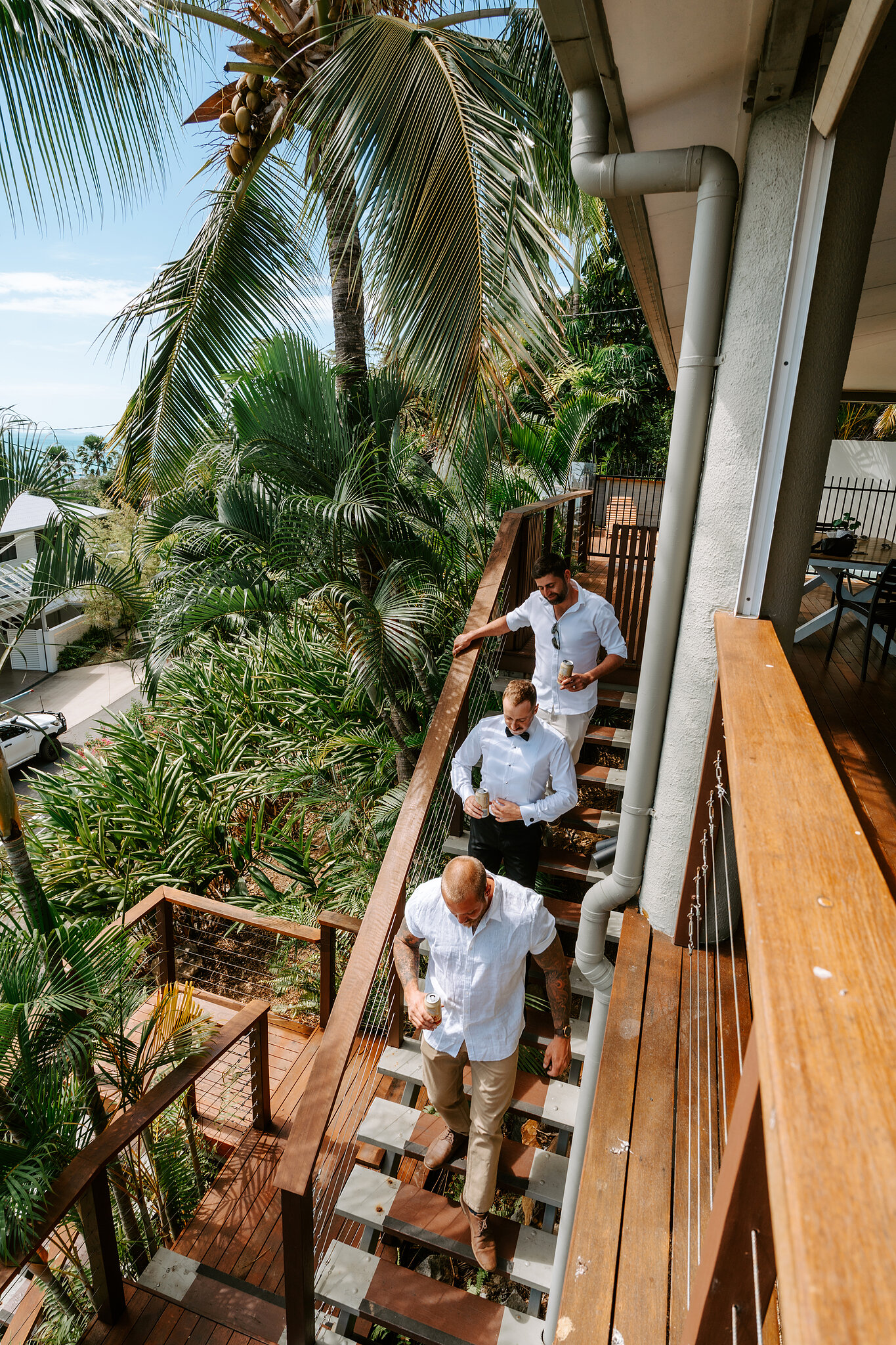 The boys head down the timber stairs of a hillside house in Airlie Beach, palms all around.