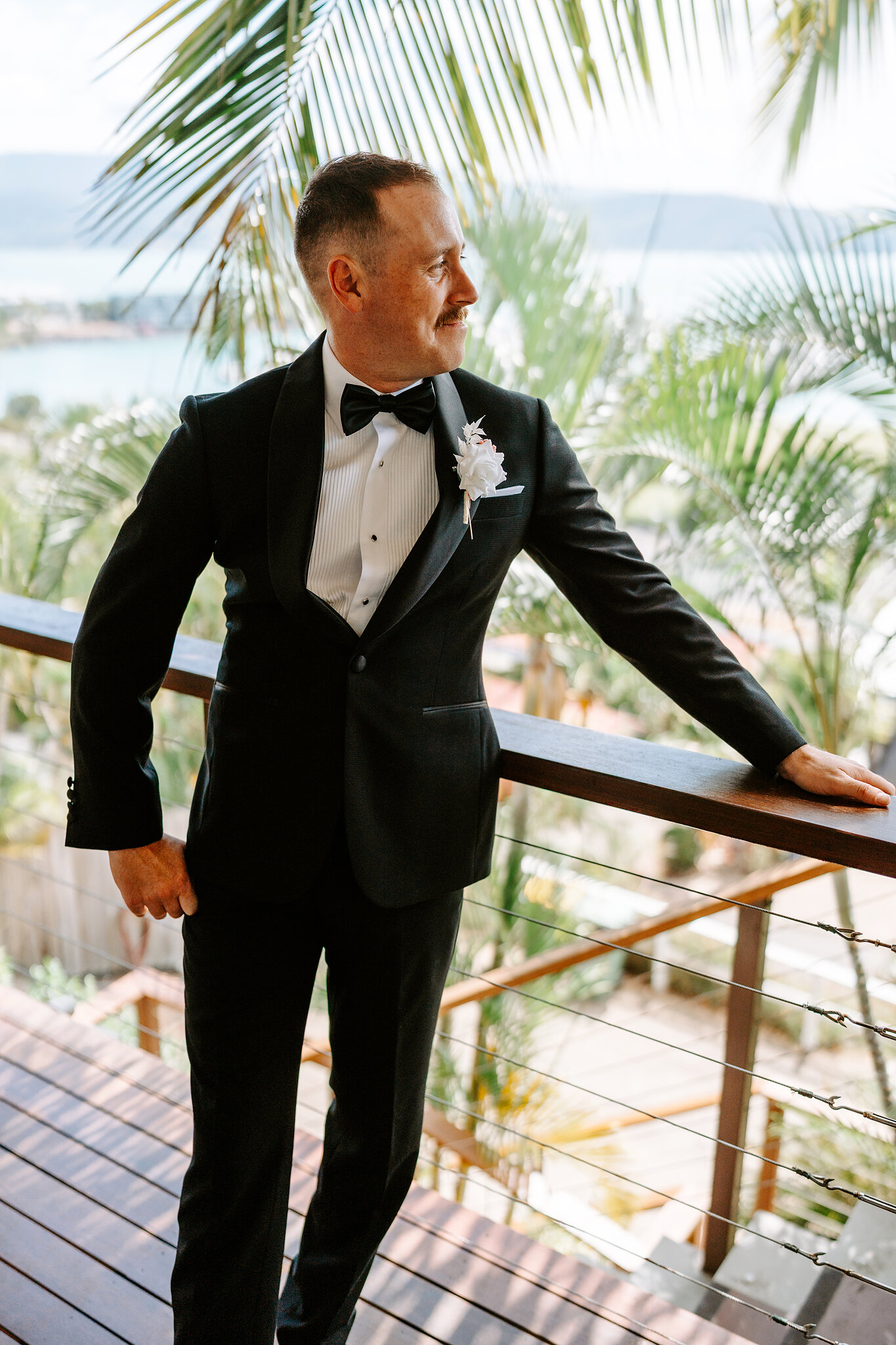Brendan leans on the balcony rail and grins, Airlie Beach spread out below.
