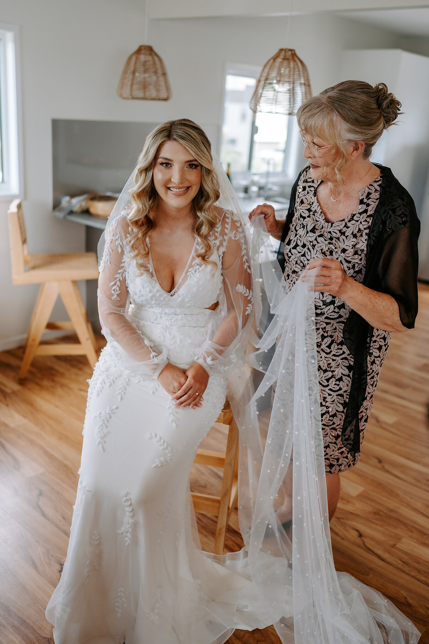 A loved one arranges Anna’s long beaded veil as she smiles from her chair.
