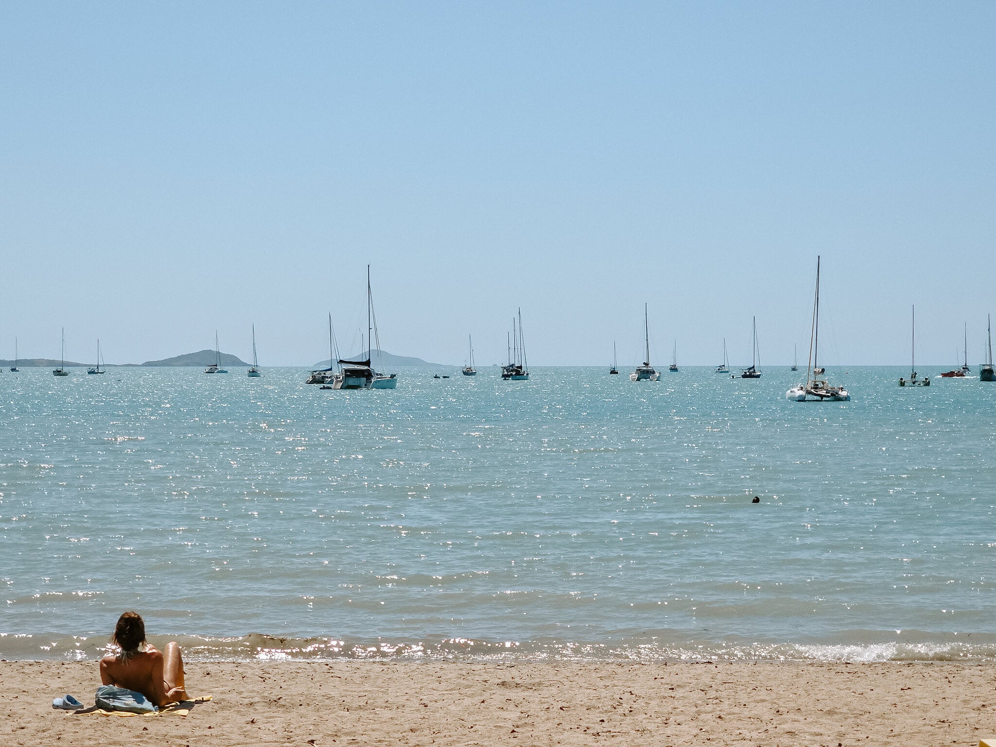 Yachts at anchor off the beach at Airlie Beach on a calm, bright day.