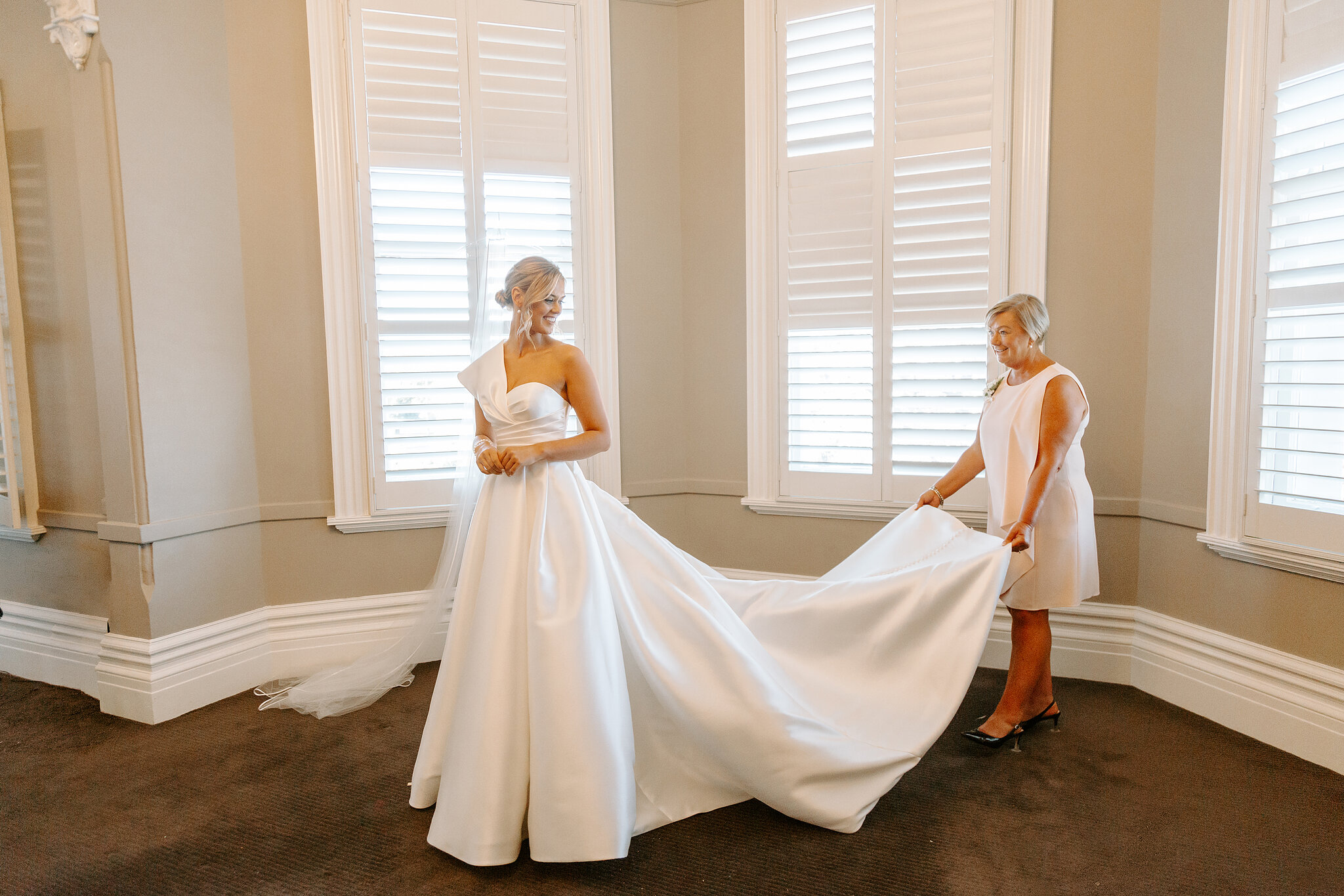 Georgie’s mum holds the dress train beside the shuttered windows at Ballarat Premier Apartments.