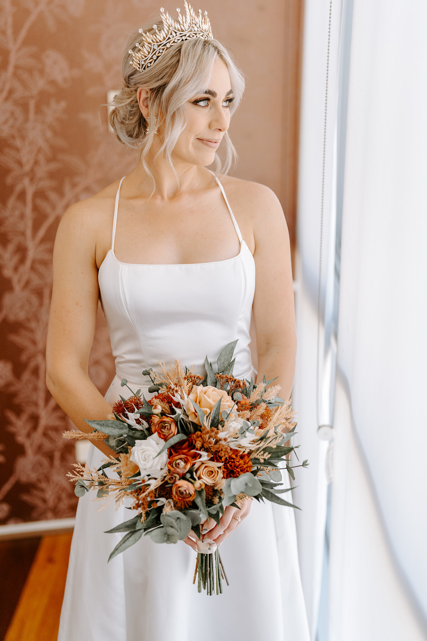 Amanda holds a bouquet of burnt orange roses, dried grasses and eucalyptus by the apartment window.