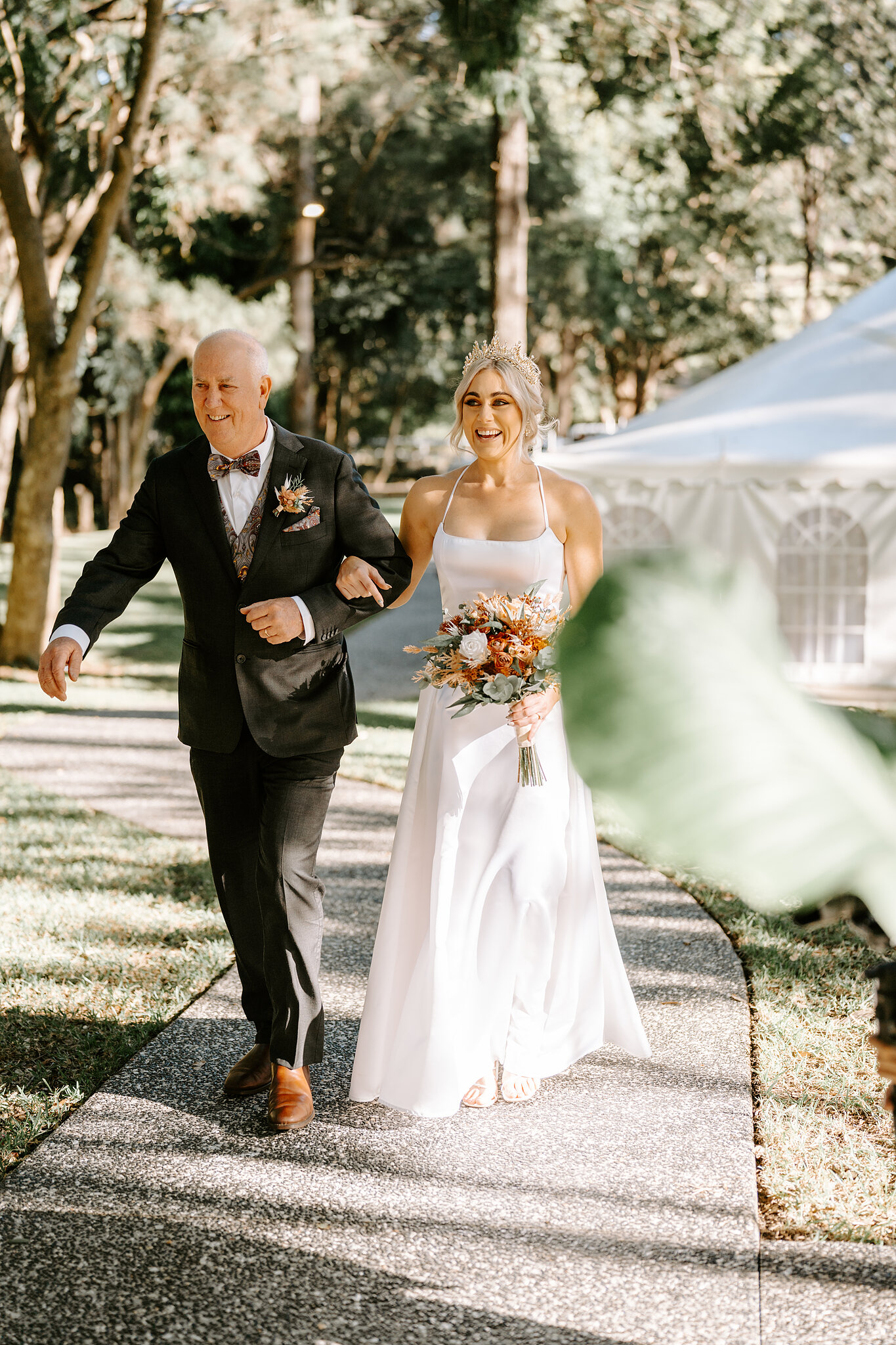 Amanda beams on her dad’s arm as they walk down the garden path, her bouquet in hand and her tiara catching the sun.