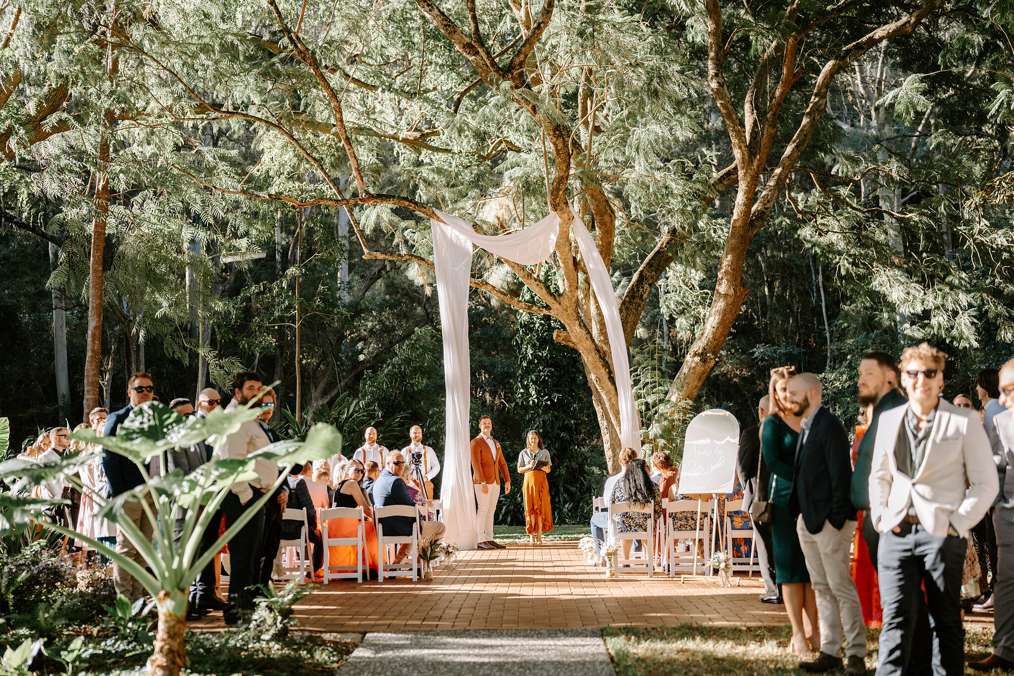Guests take their seats under the rainforest canopy as white silk drapes from the Jacaranda Tree.