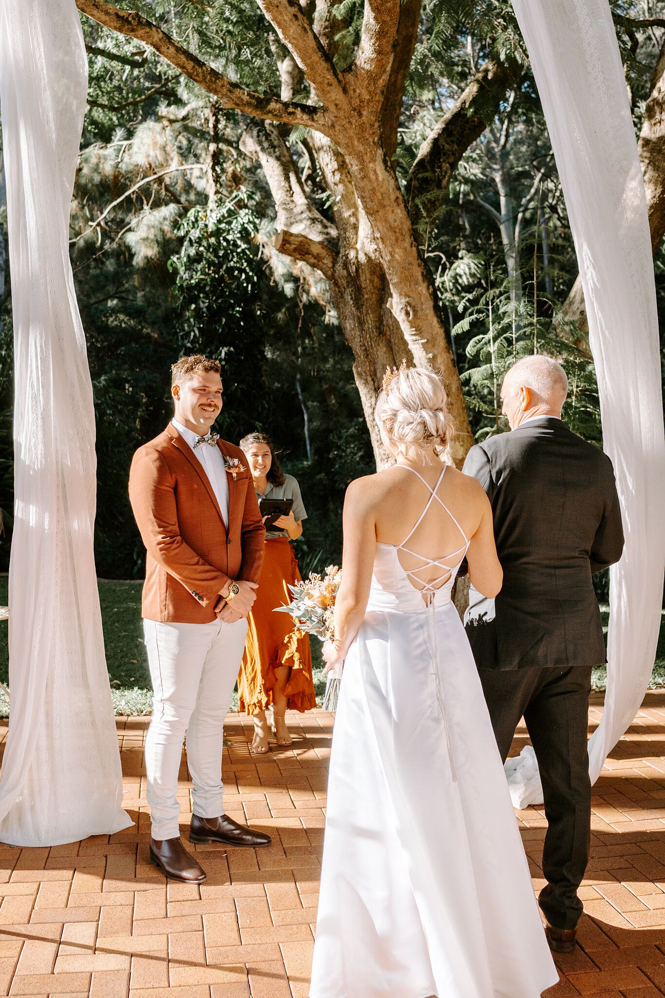 Amanda reaches the front, the lace-up back of her gown framed by white silk drapes.