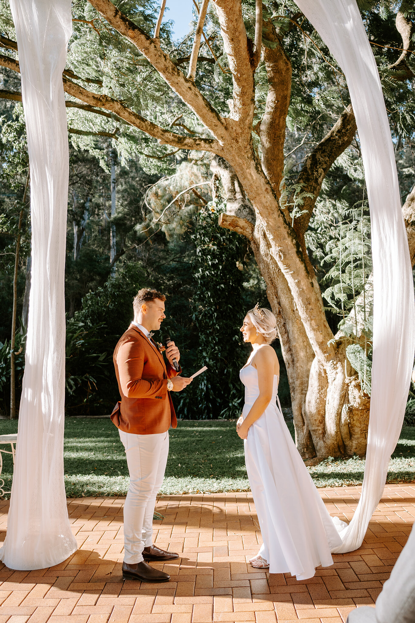 Patrick reads his vows into the microphone as Amanda listens under the drapes.