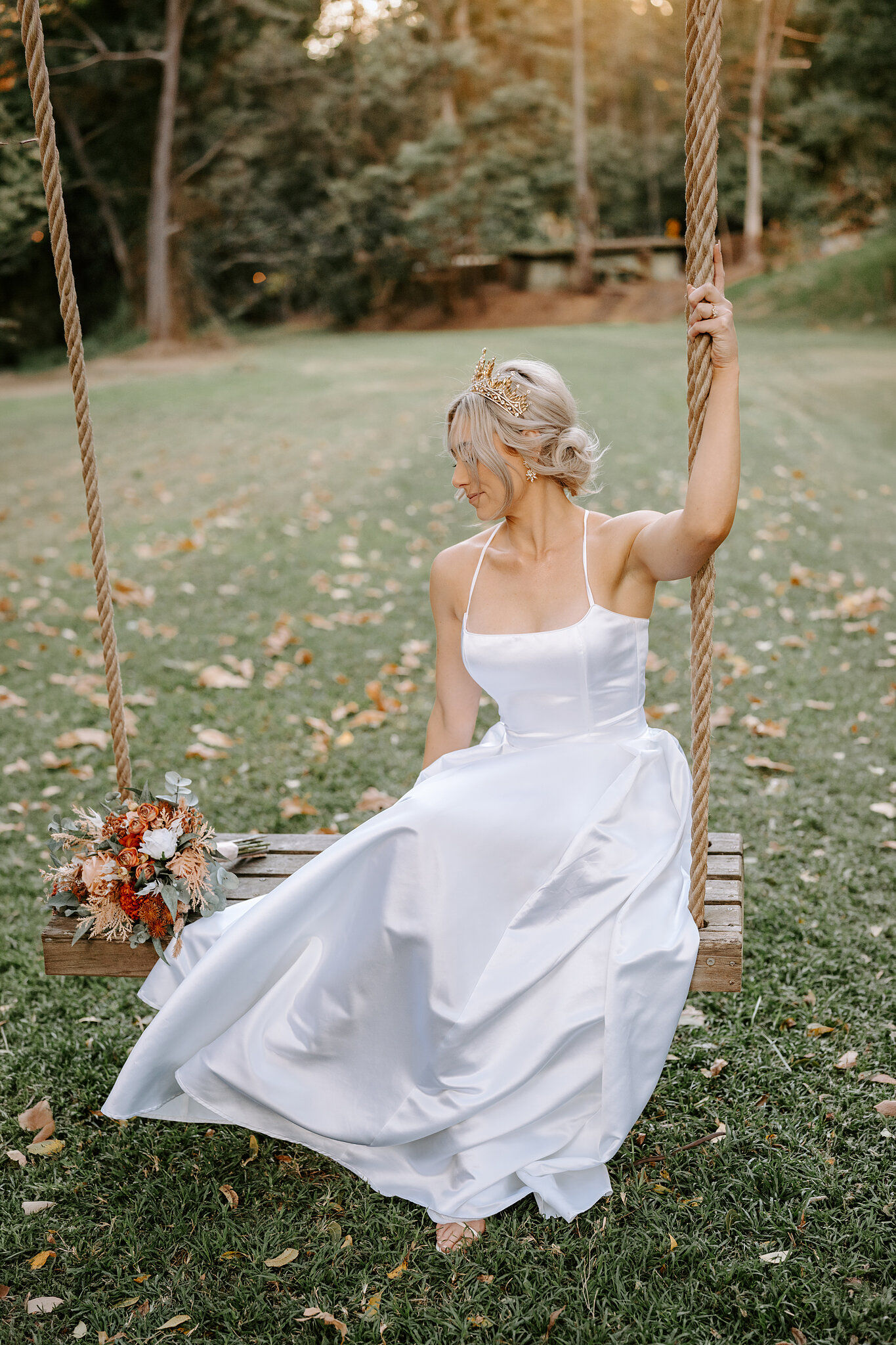 Amanda sits on a rope swing on the leafy lawn, her bouquet resting on the timber seat beside her.