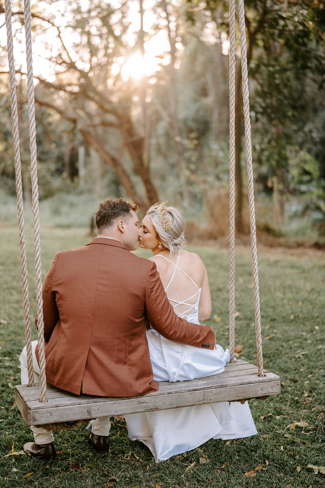 Amanda and Patrick share a kiss on the rope swing as late sun breaks through the trees.