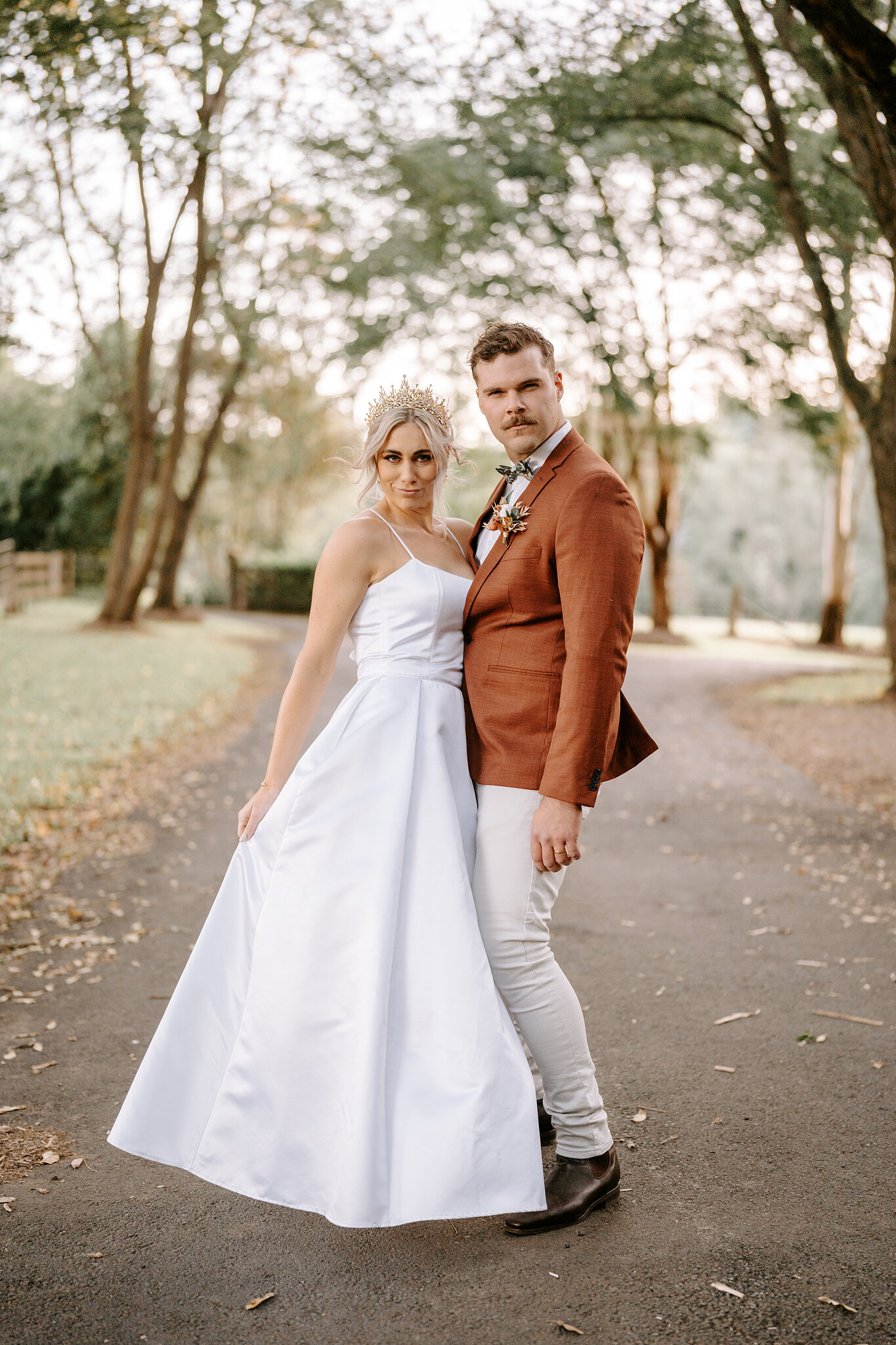 Amanda and Patrick stand together on the leaf-scattered driveway, looking straight down the lens.