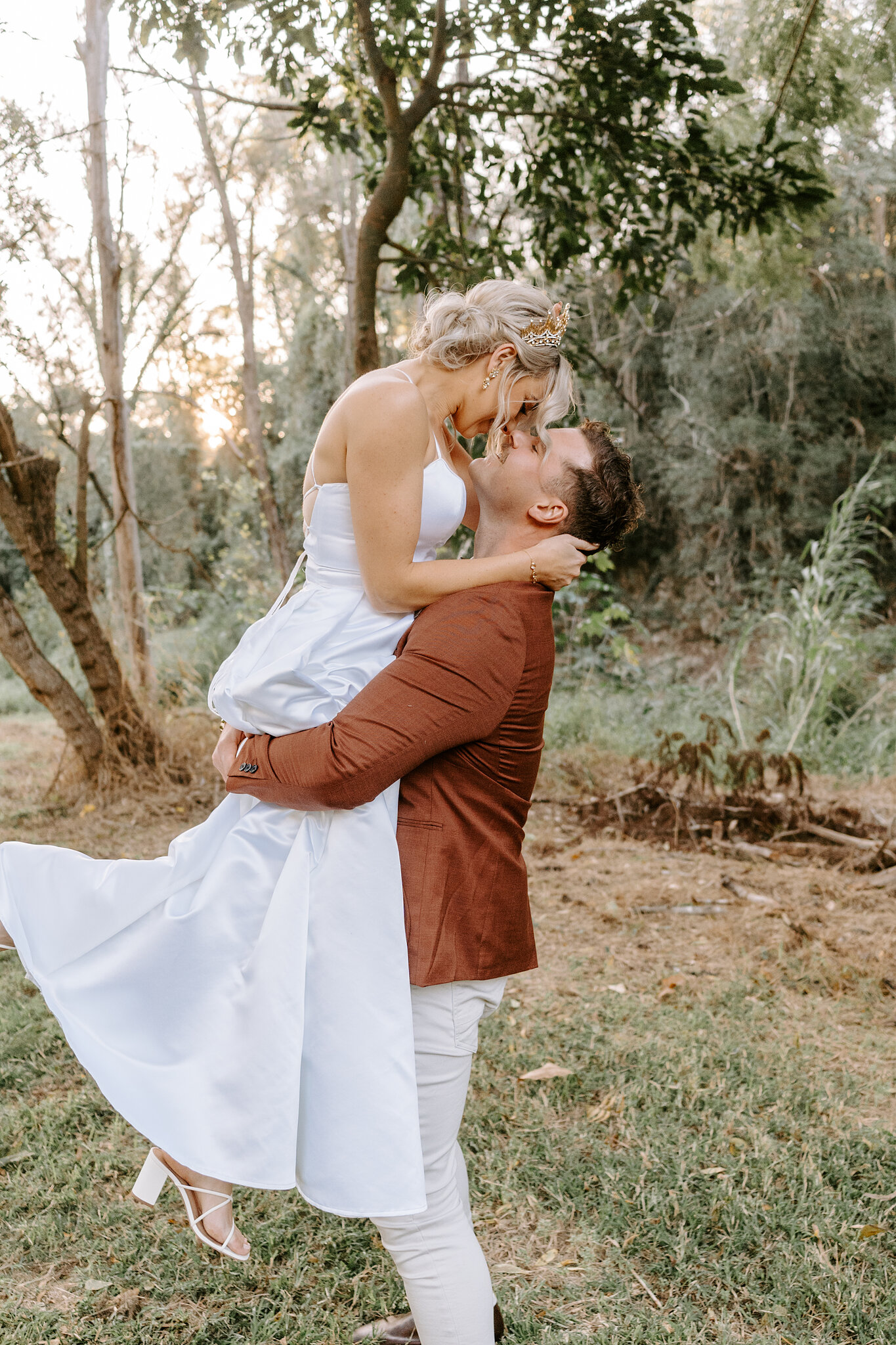 Patrick lifts Amanda off her feet for a kiss, her heels kicking up beside the bush.