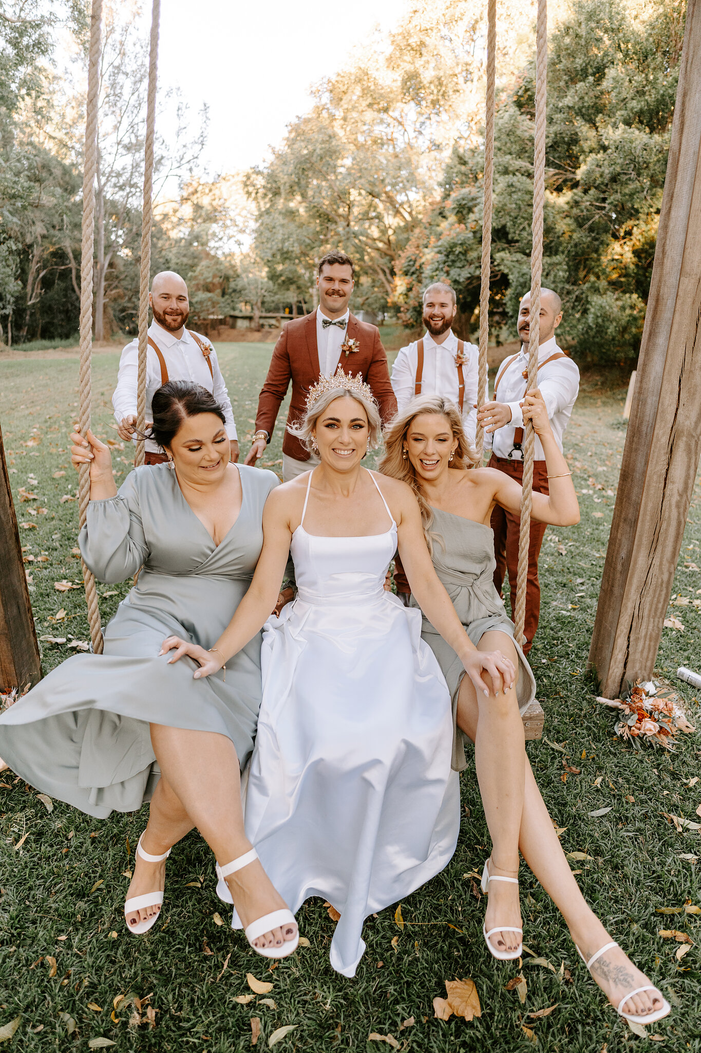 Amanda sits on the rope swing between her bridesmaids, the groomsmen standing behind.