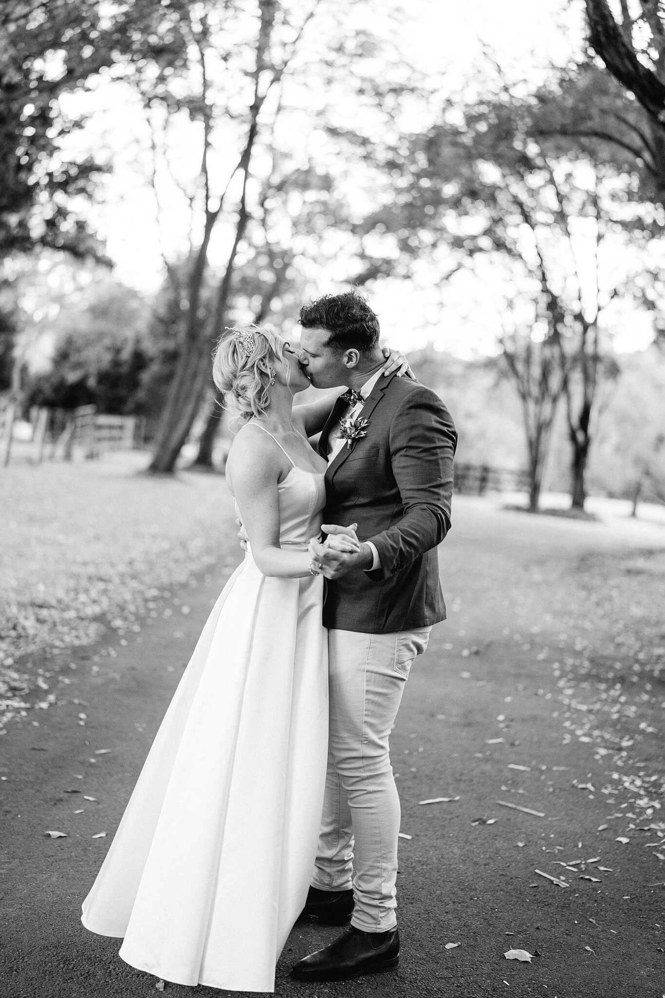 Amanda and Patrick kiss on the driveway, leaves scattered along the path.