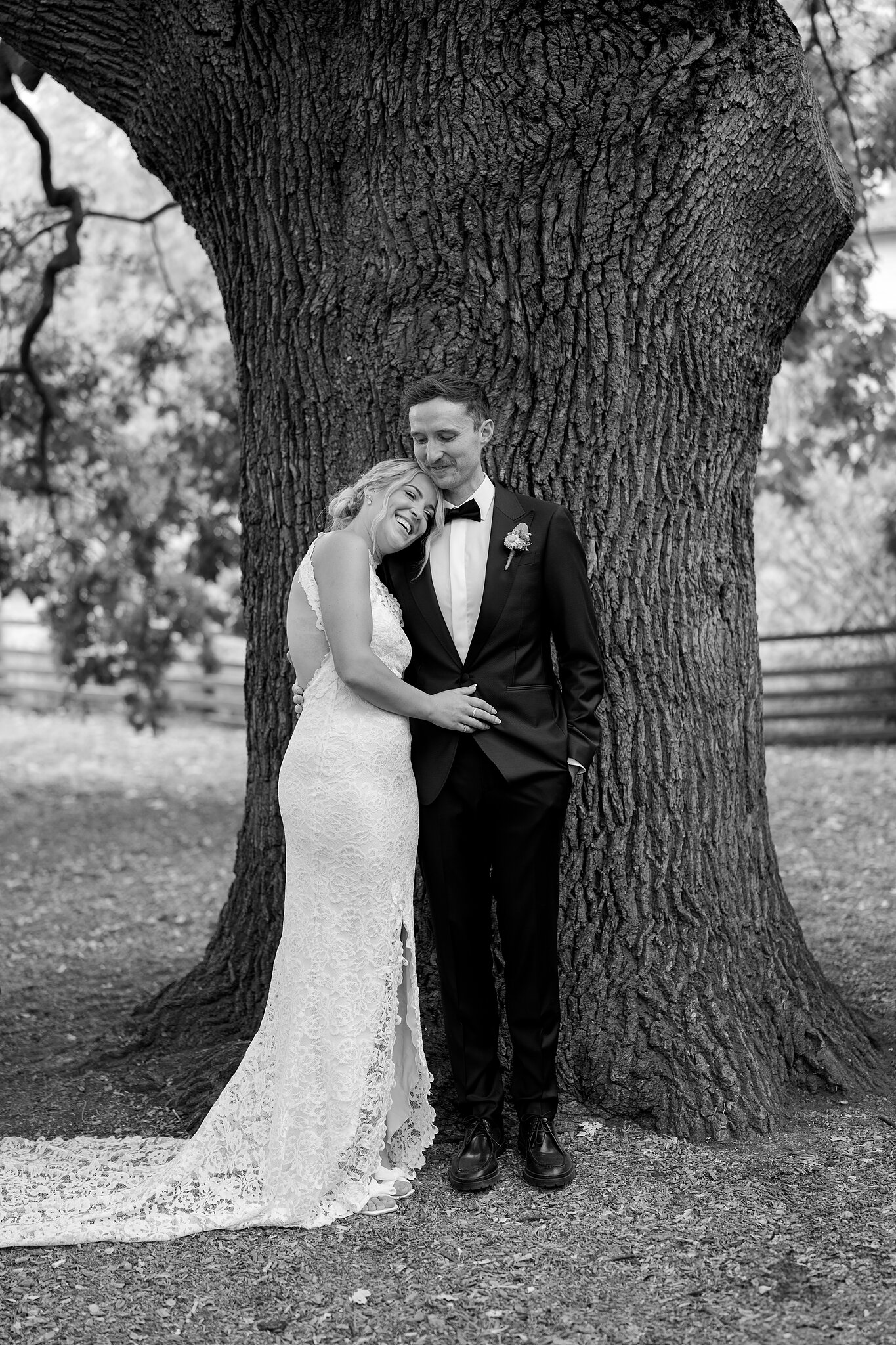 Emma rests her head on George’s chest beneath the giant oak, in black and white.