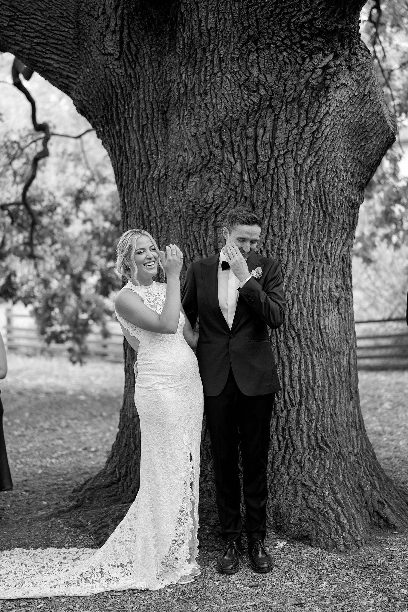 George wipes away a tear as Emma laughs beside him under the oak, in black and white.