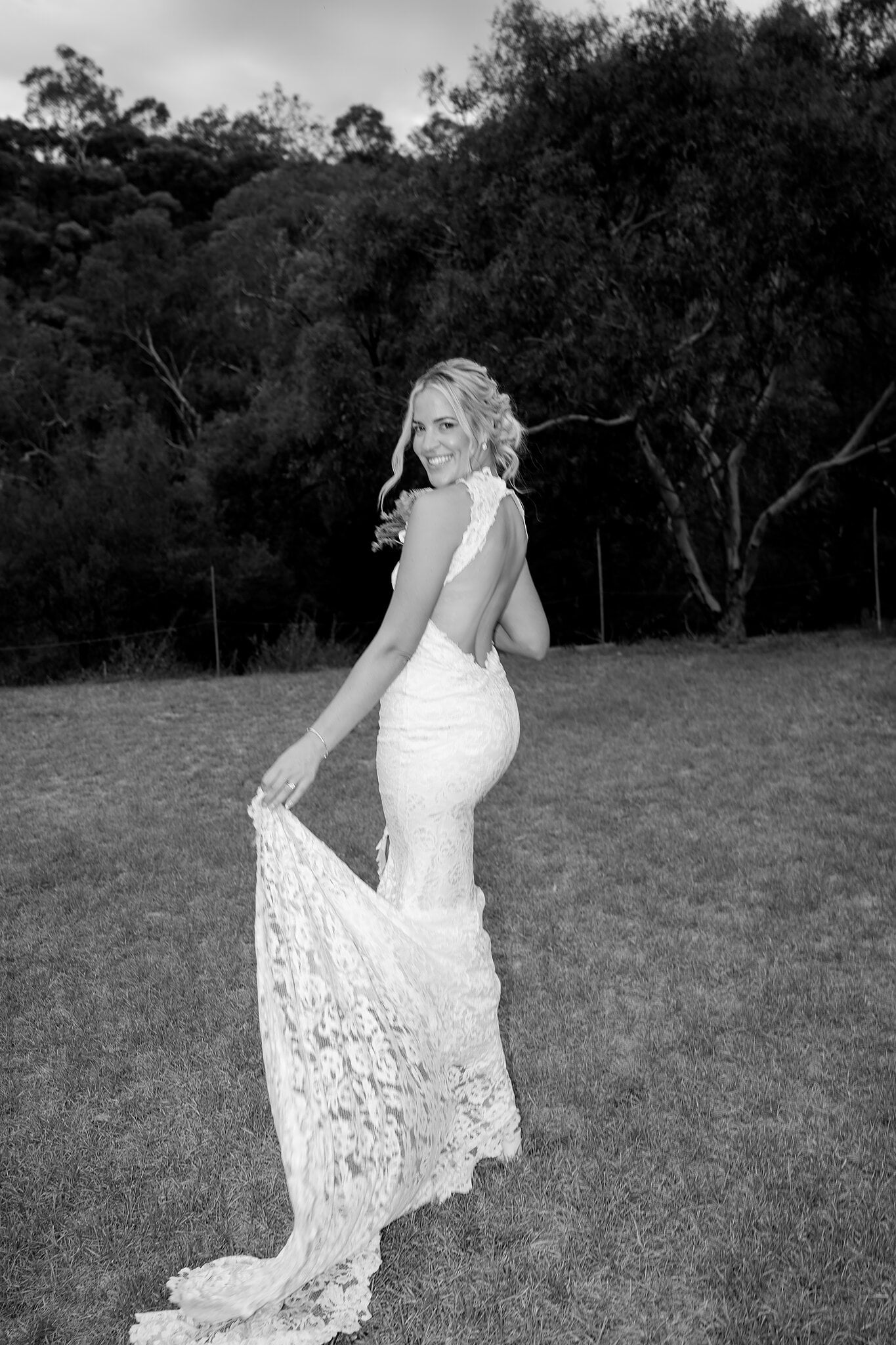 Emma lifts her lace train and looks back across the paddock, in black and white.