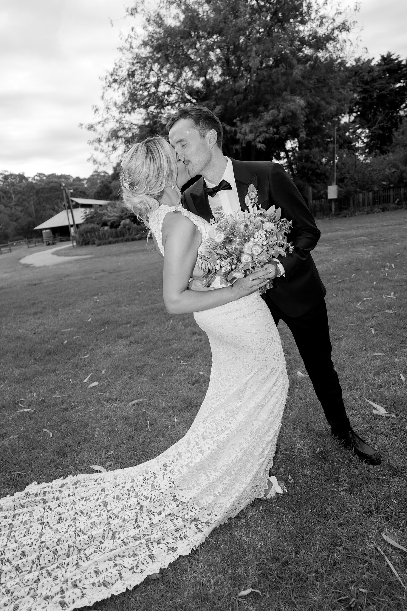 George kisses Emma as she leans back, her lace train curling across the lawn.