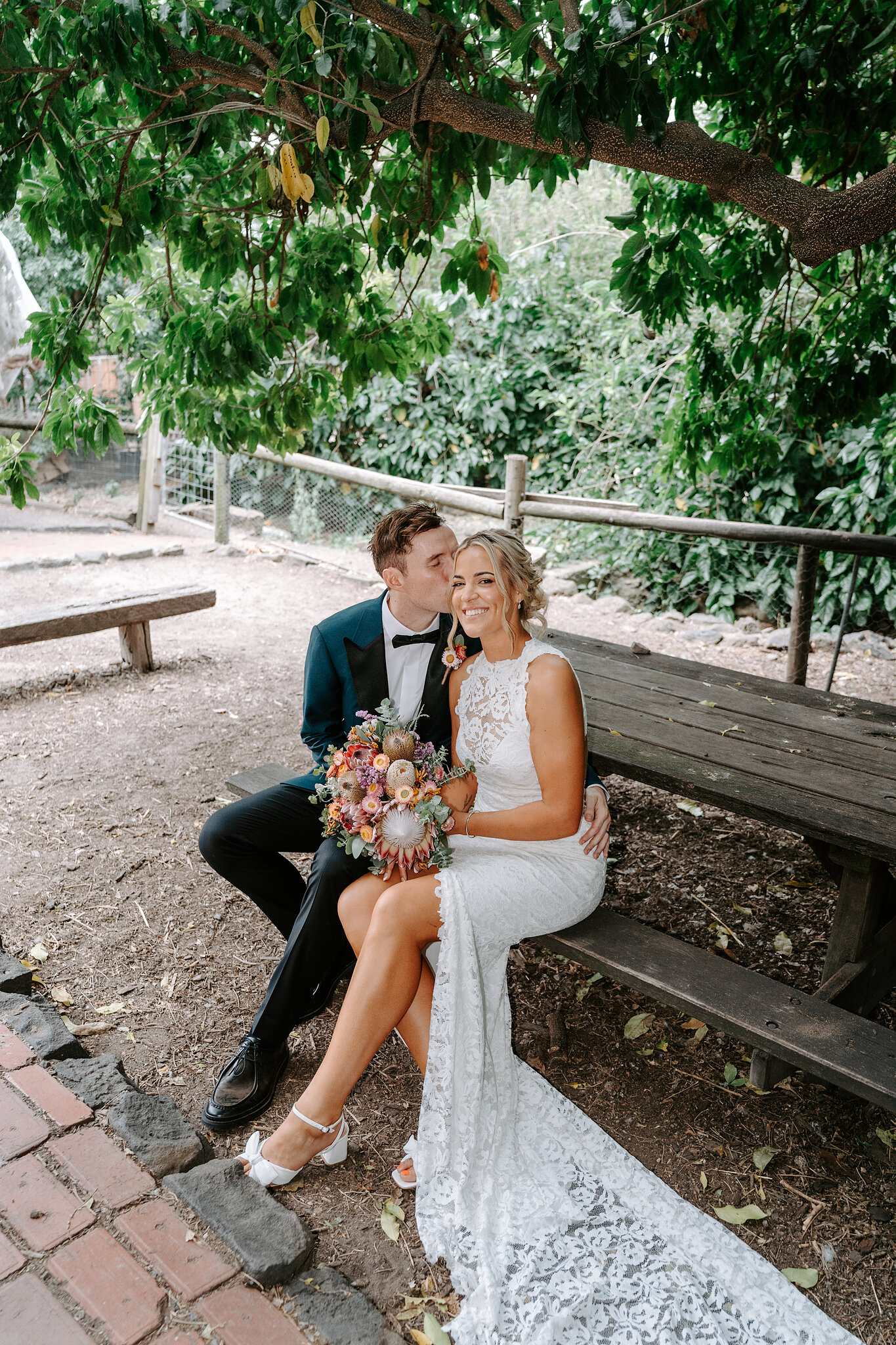 Emma and George sit together on a timber bench under the trees.