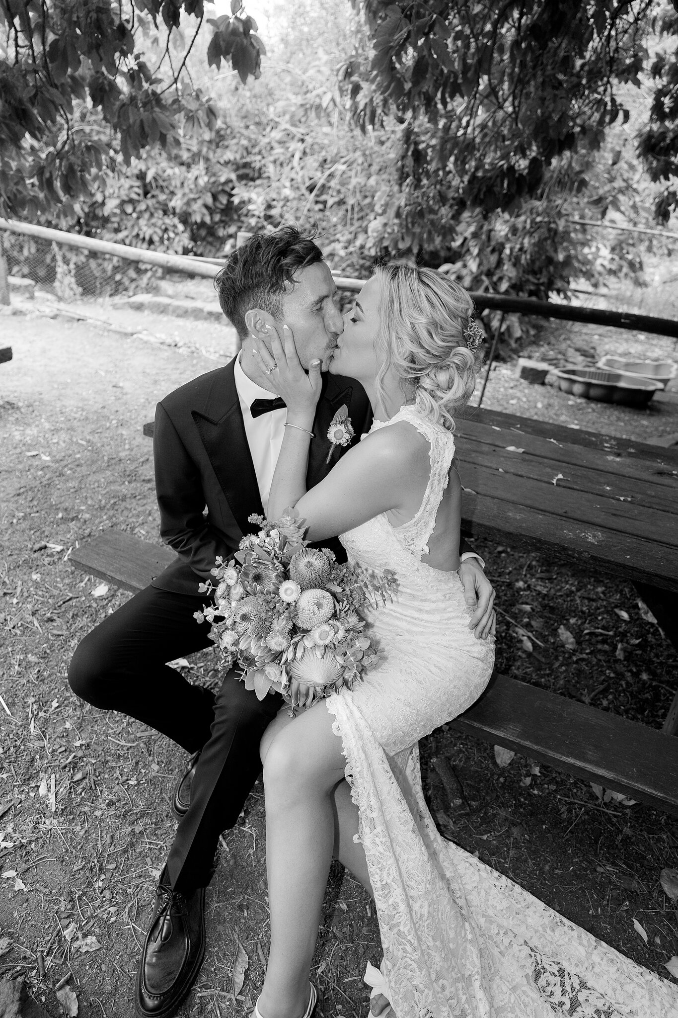 Emma and George kiss on the timber bench, in black and white.
