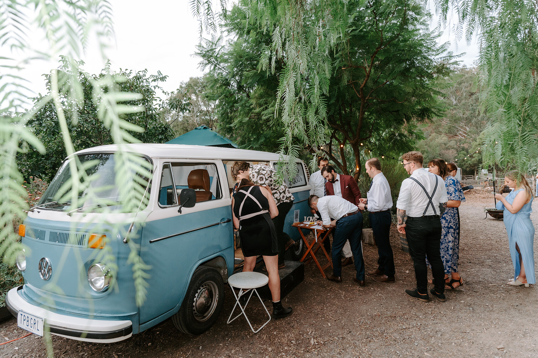 Guests gather at a blue vintage Kombi van bar under the pepper trees.