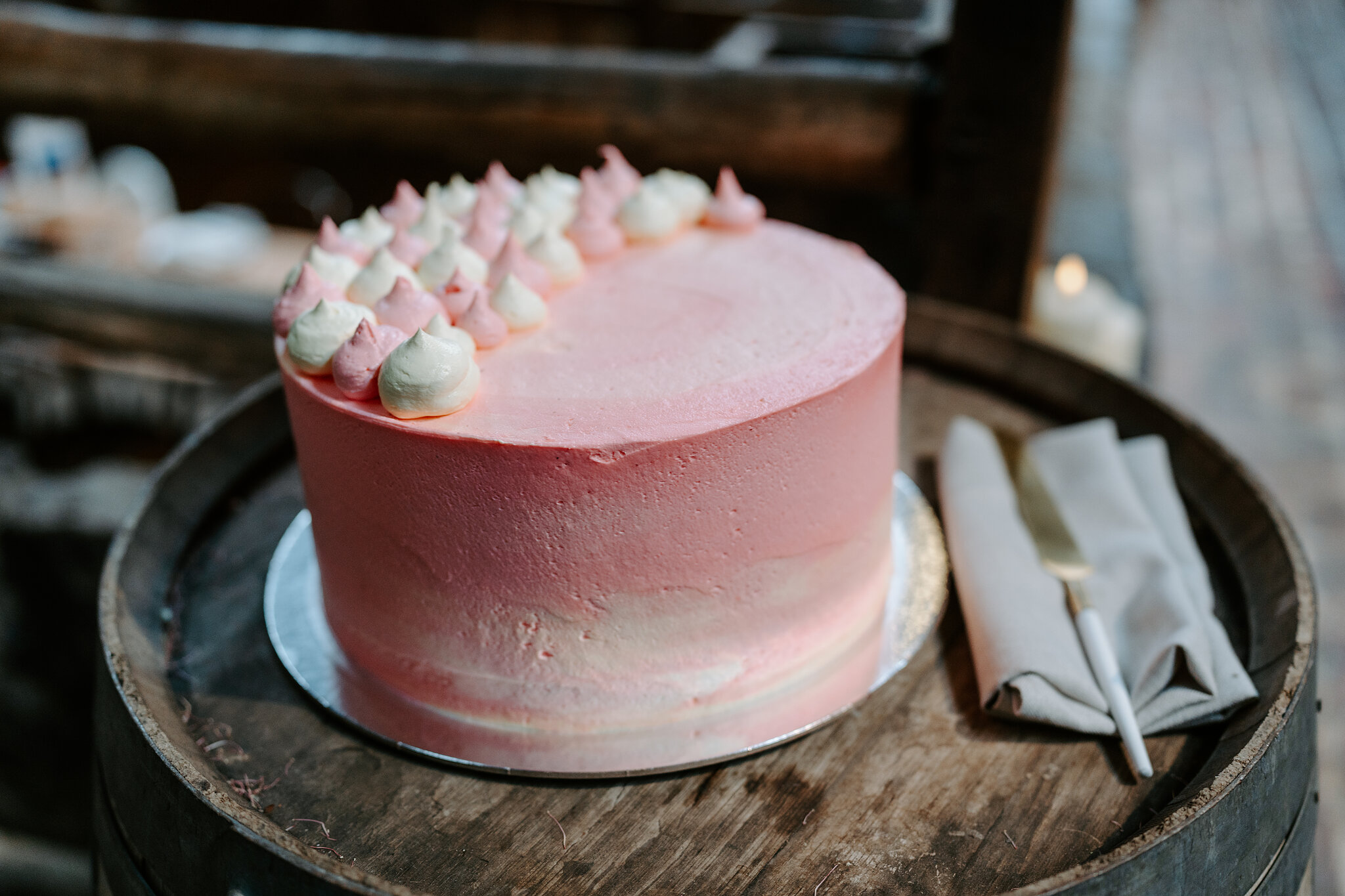 A pink ombre wedding cake topped with meringue kisses sits on a timber barrel.