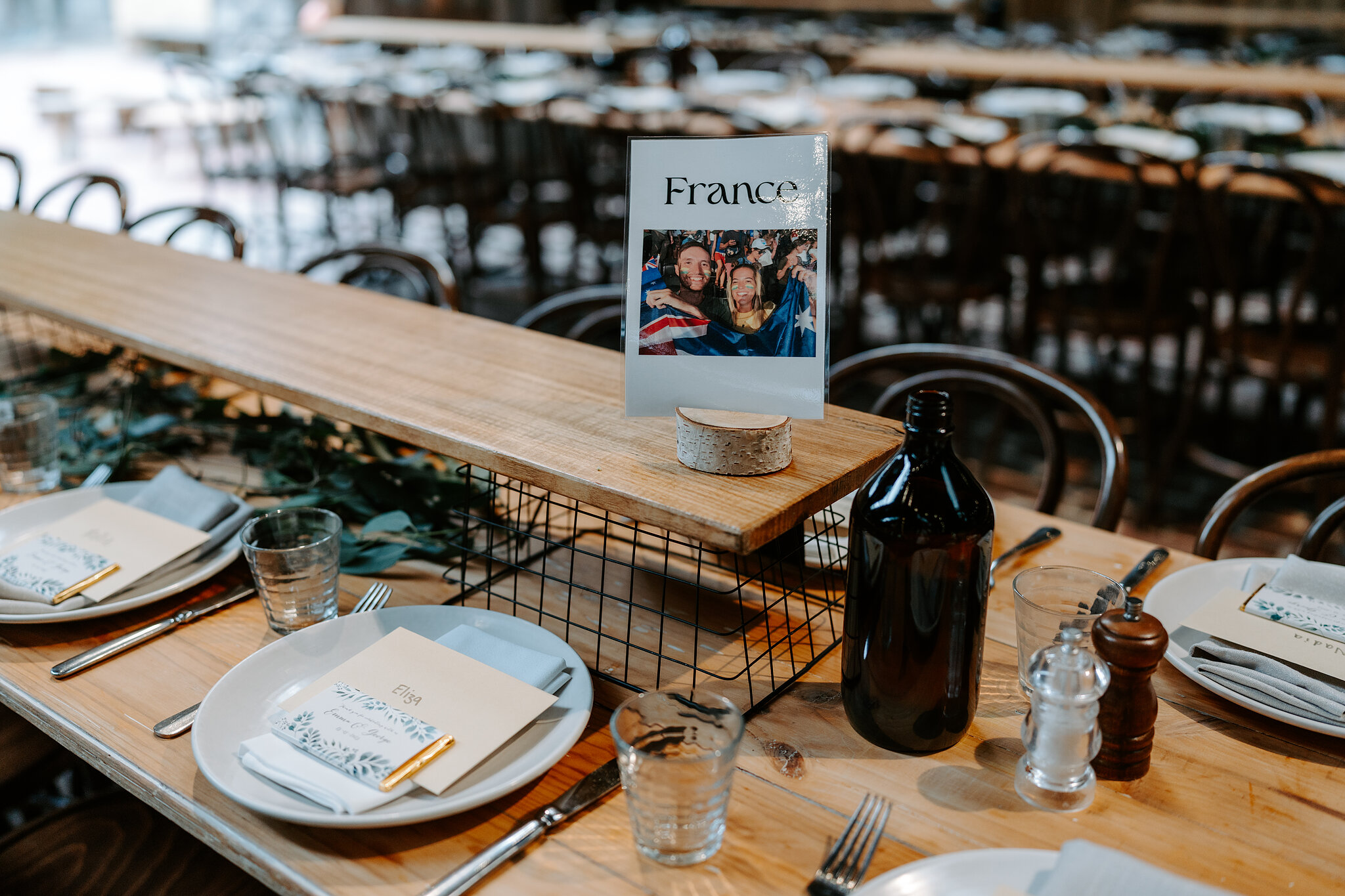 Long timber tables in the Barn, with a France table card and a travel photo.