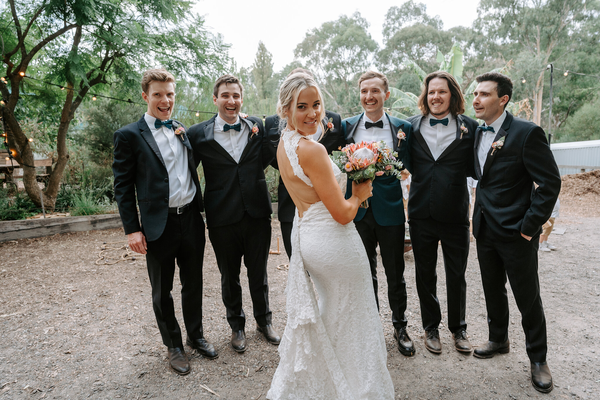 Emma and George with the groomsmen in black tuxedos in the farmyard.