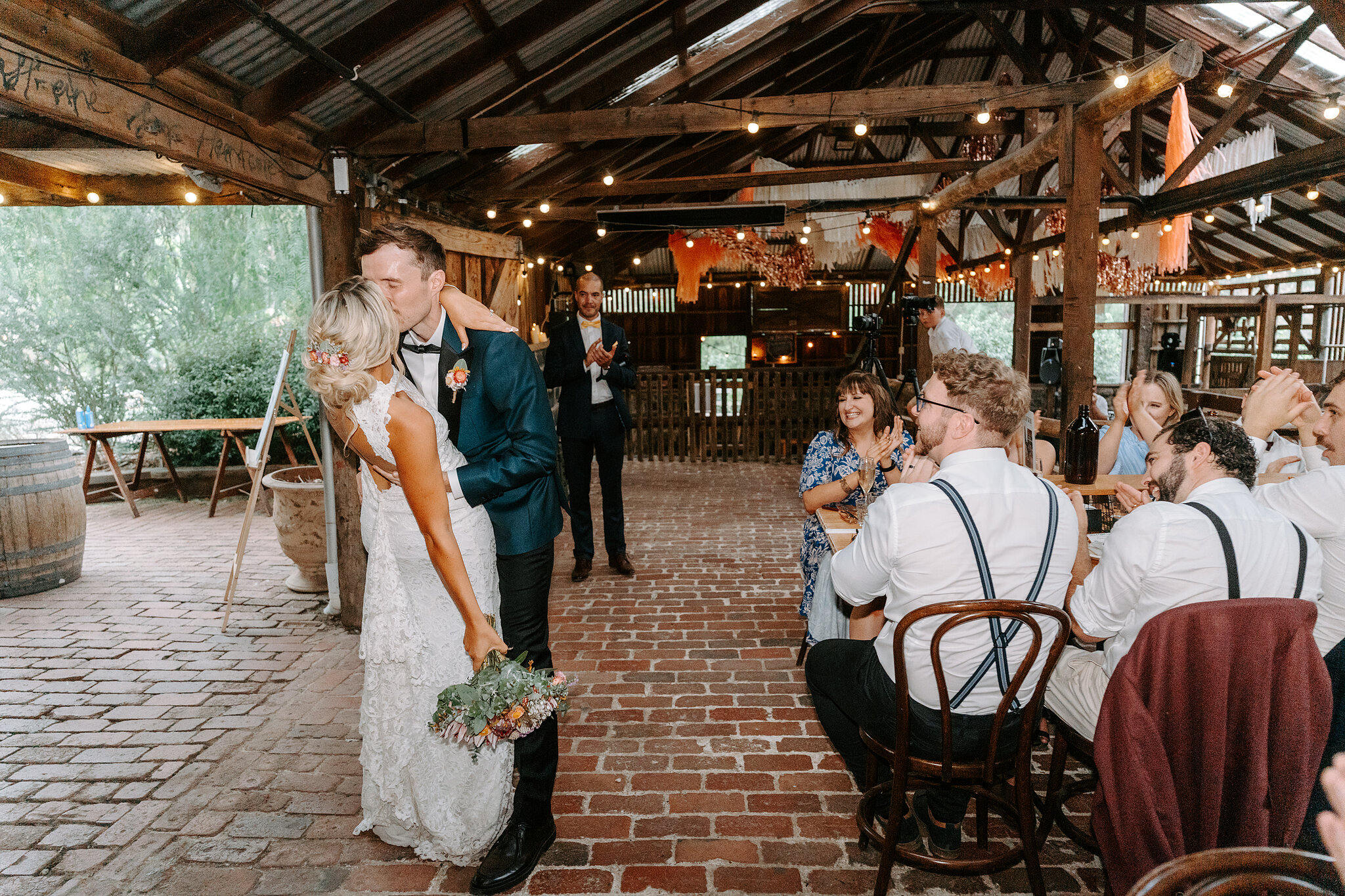 Emma and George walk into the Barn past guests at the long tables.