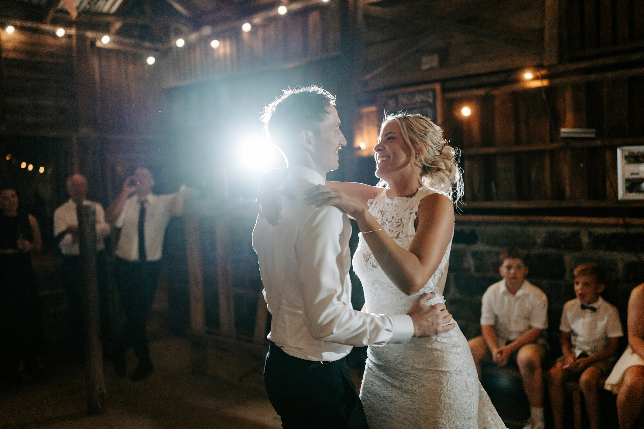 Emma and George laugh through their first dance as guests watch from the benches.