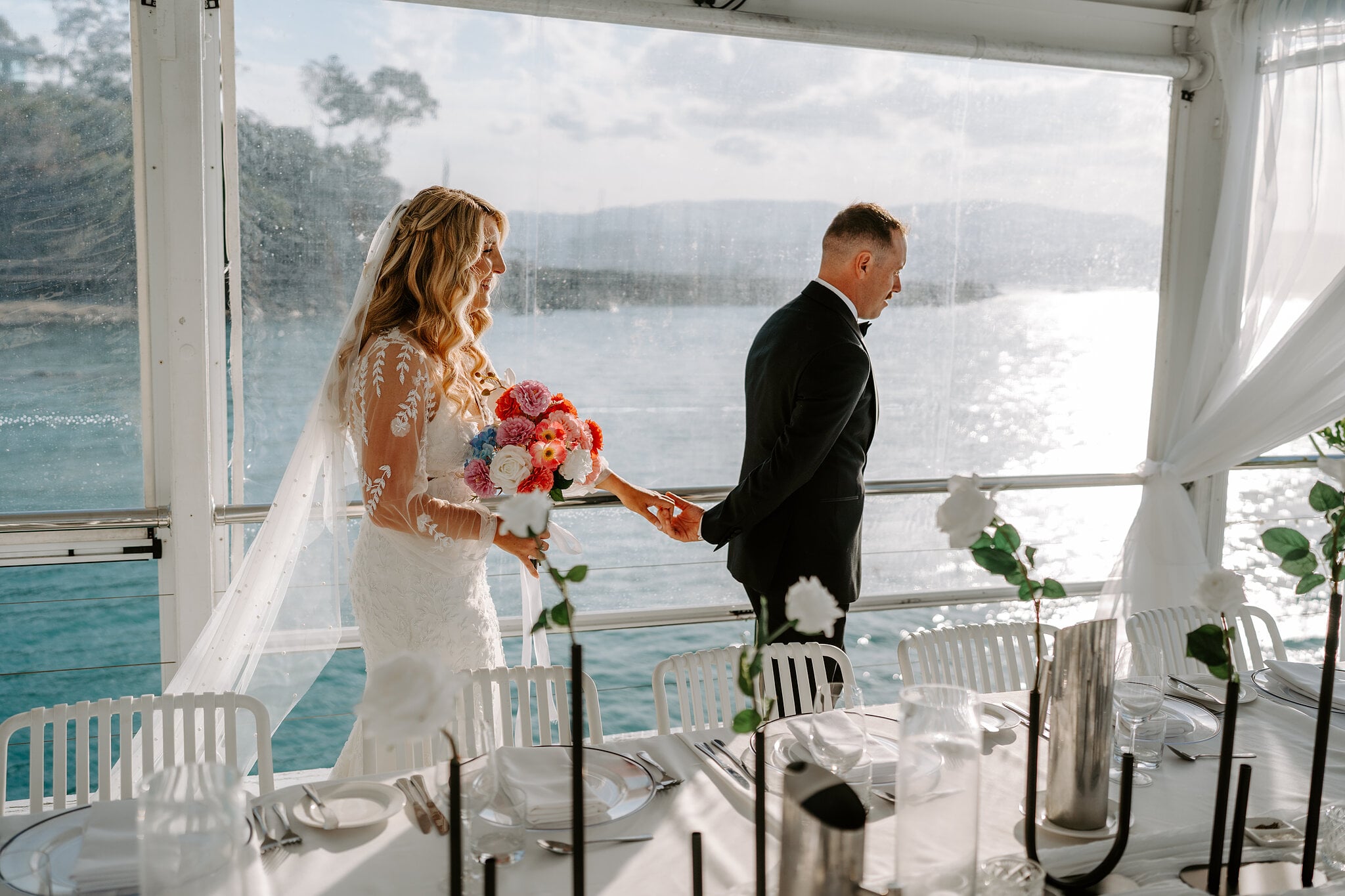 Anna and Brendan step into their reception under the jetty marquee, tables set over the water.