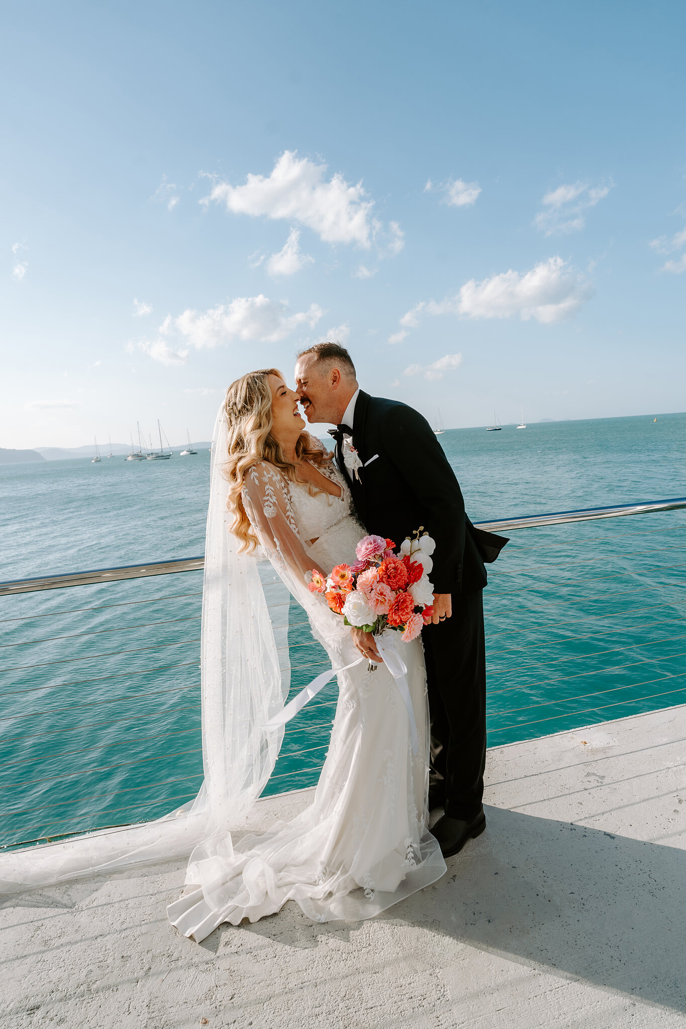 Brendan kisses Anna on the jetty, turquoise water all around them.